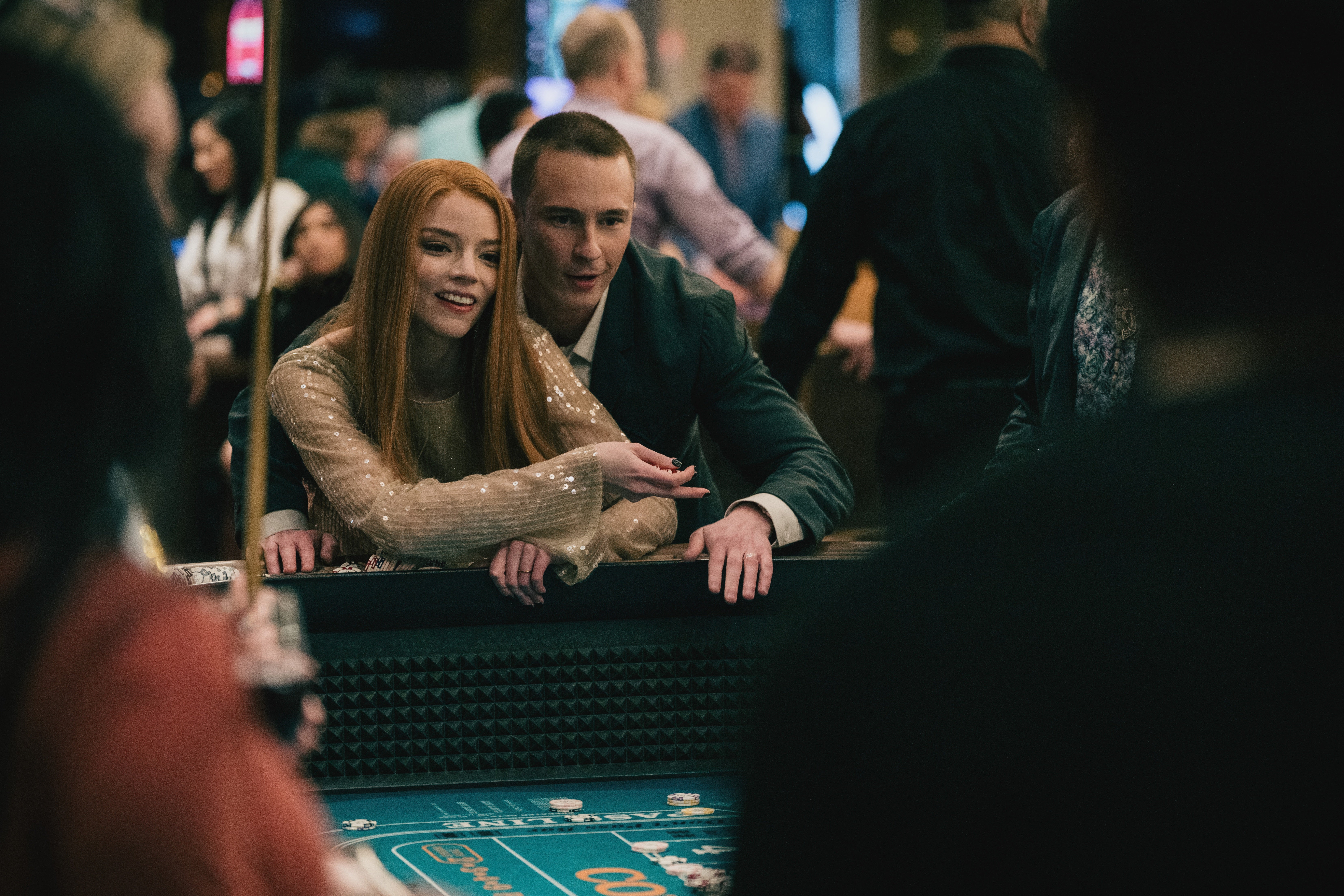 Two people enjoying a casino game, one in a sparkling top and the other in a suit, surrounded by a crowd at the gaming table