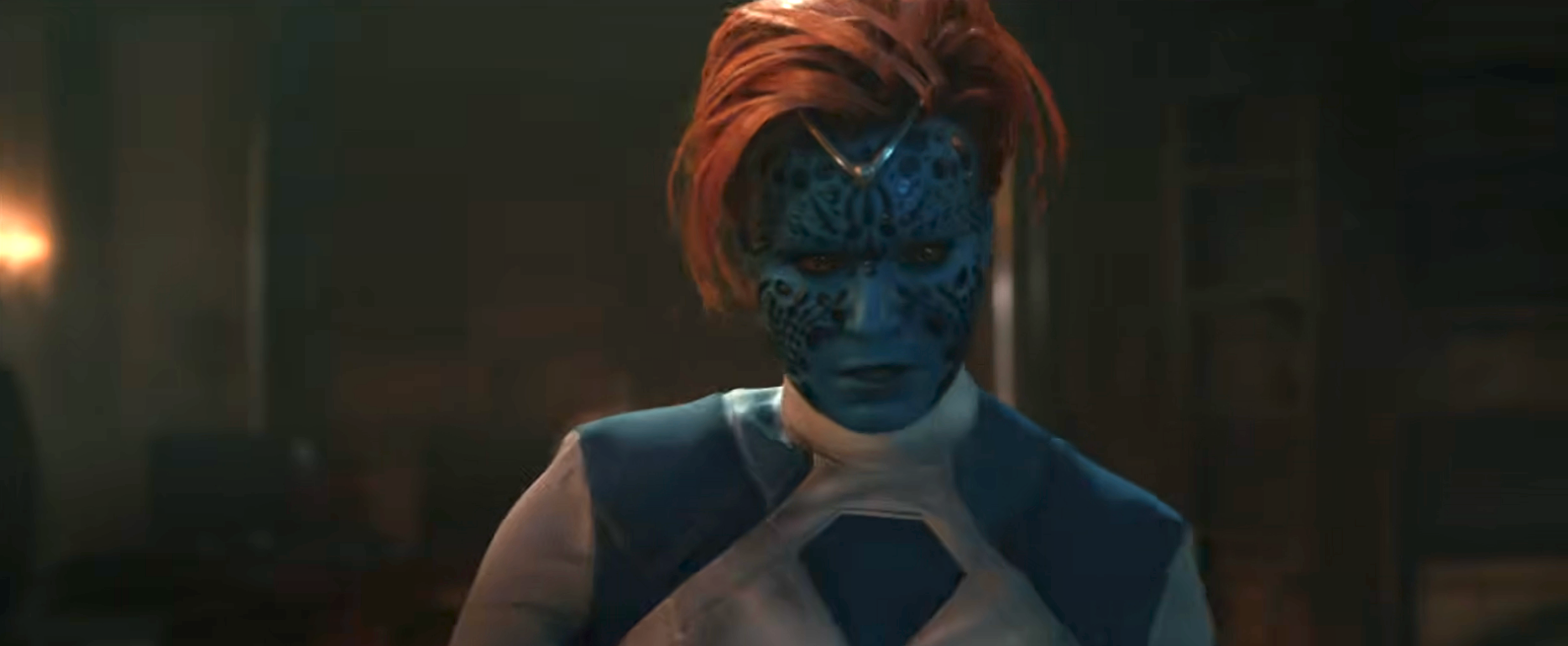 Character in a sci-fi film with blue patterned skin and red hair, wearing a futuristic outfit