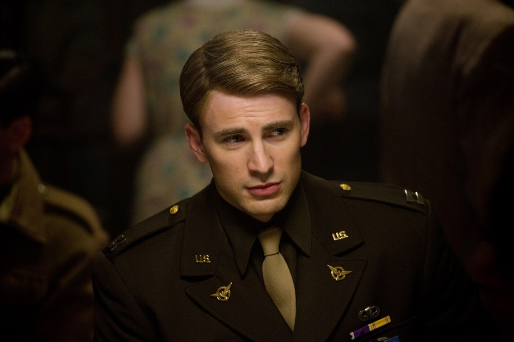 A person in a military uniform is looking to the side in a thoughtful manner