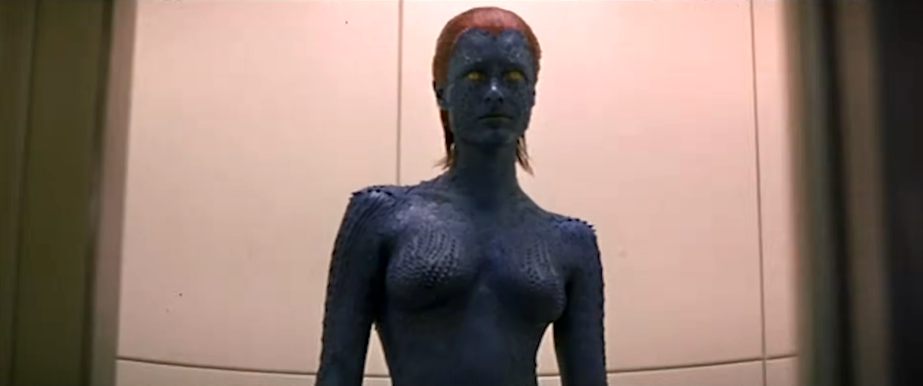 A character in detailed body paint and prosthetics stands, resembling a sci-fi or fantasy figure with a textured, otherworldly skin appearance