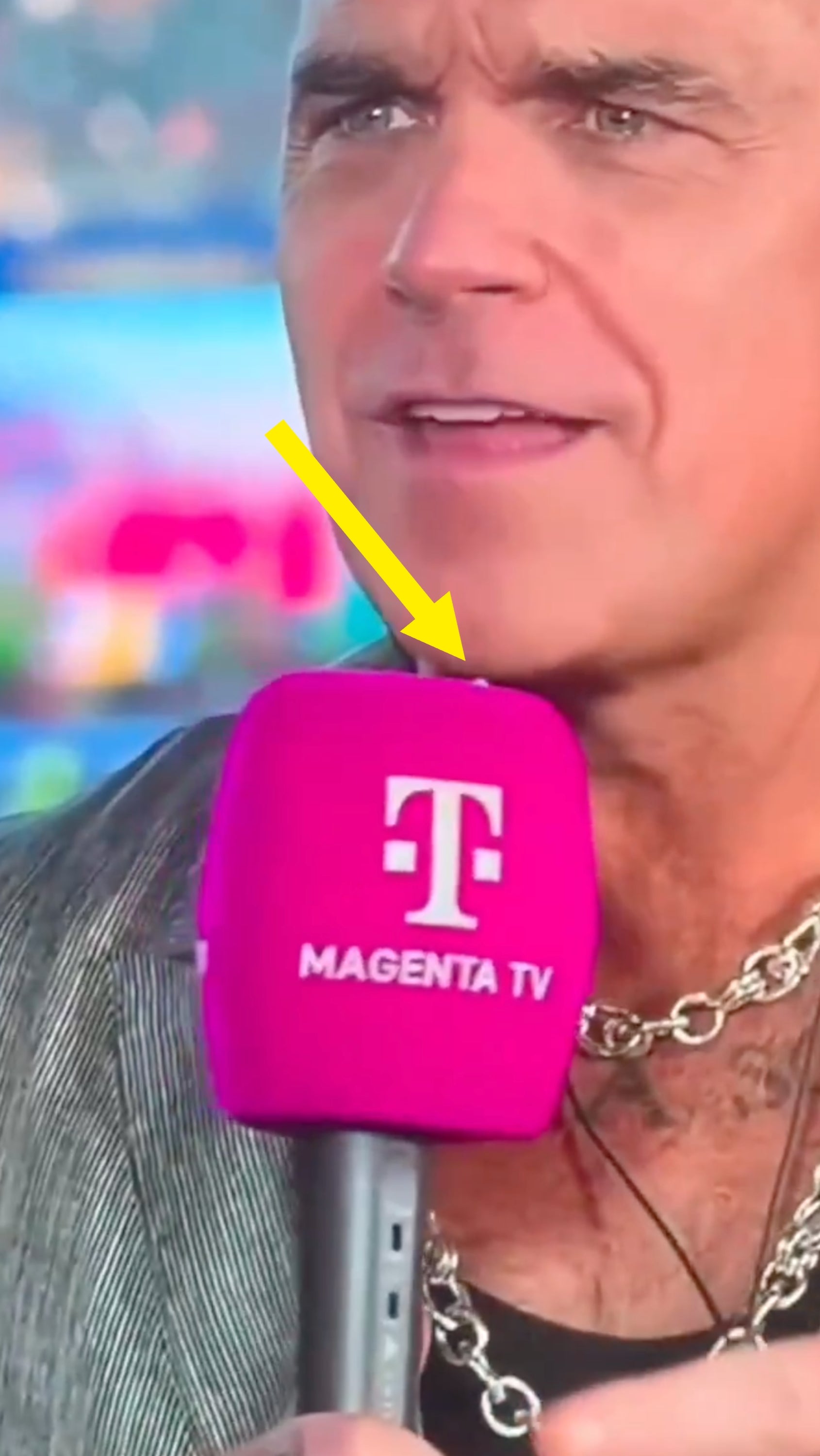 Selebriti dengan kalung rantai memegang mikrofon magenta berlabel 