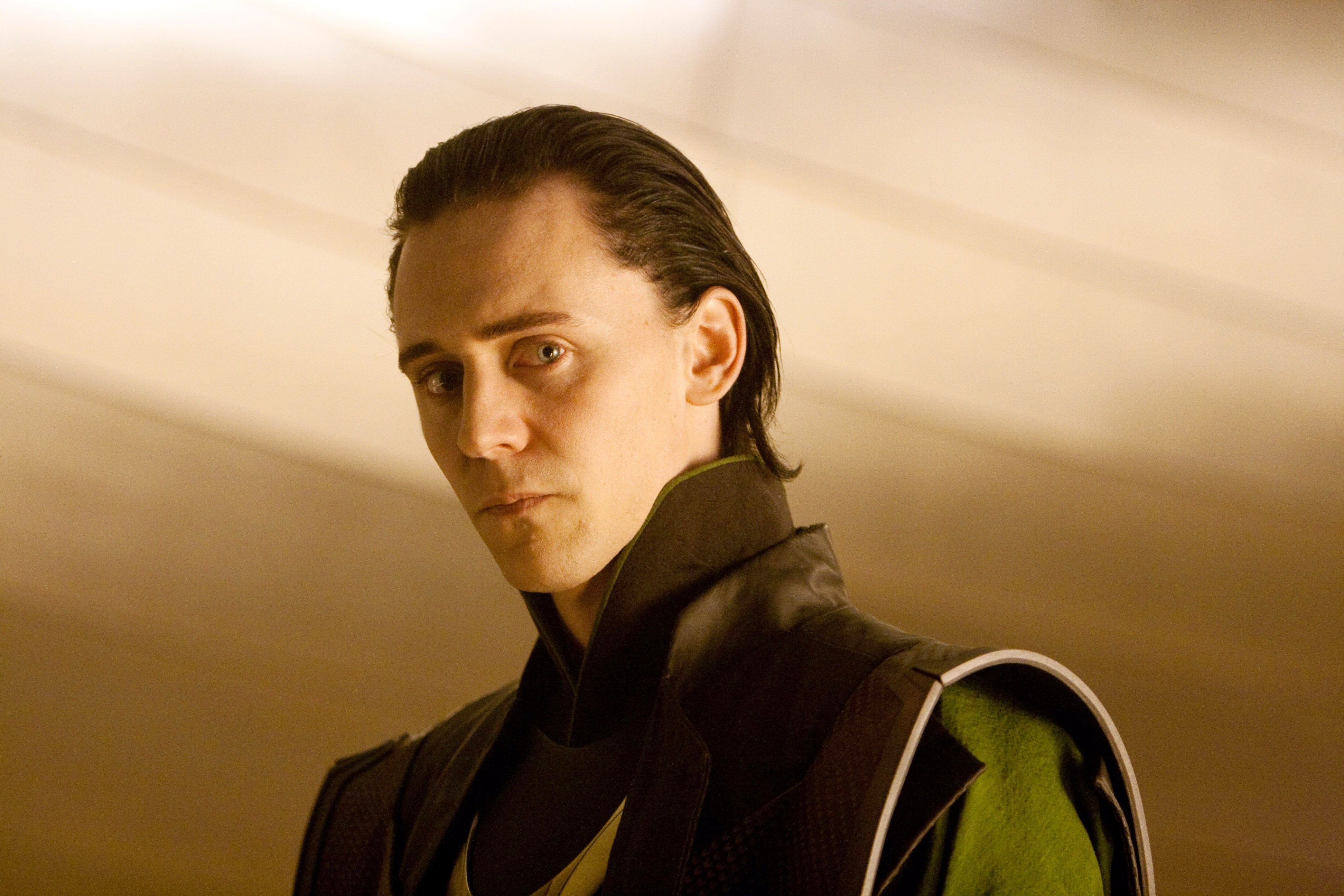 Person dressed as a character with slicked-back hair, wearing a dark, structured outfit with shoulder accents