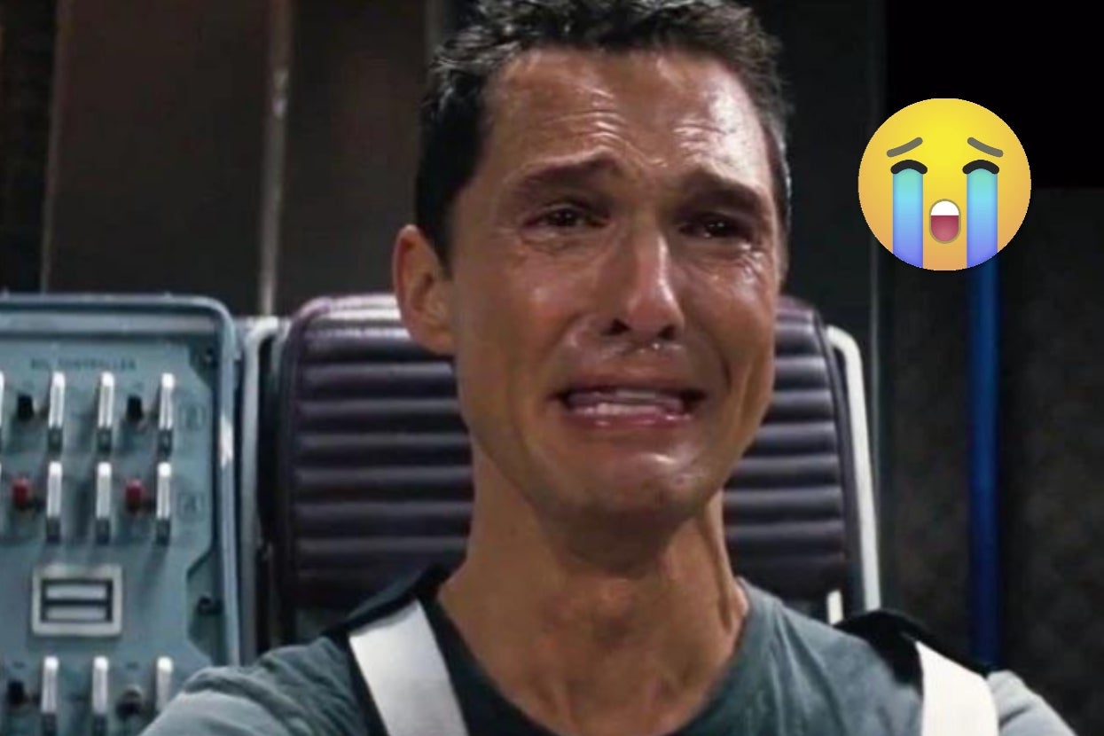 A tearful person in a futuristic setting, wearing a T-shirt and harness, with a crying emoji added to the image
