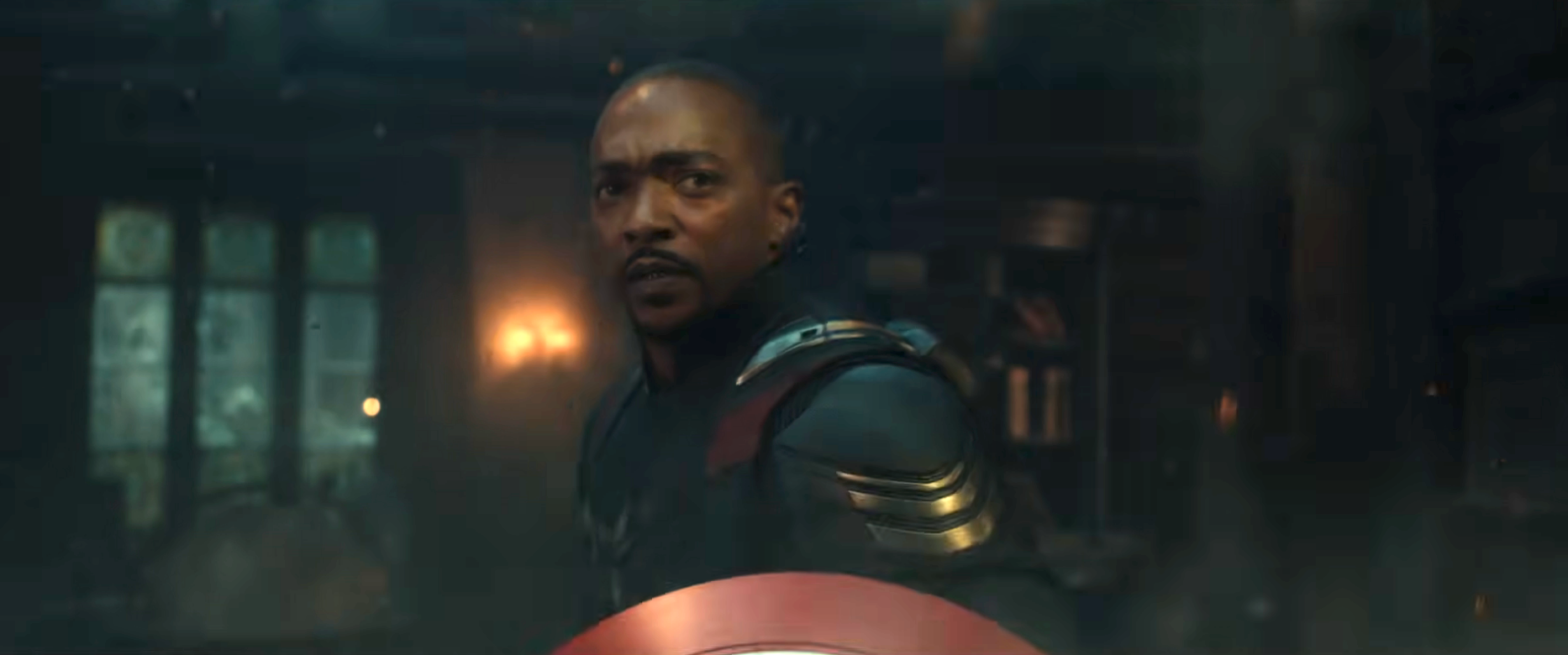 A person in a superhero costume holding a shield is in an intense setting with focused expression and dramatic lighting