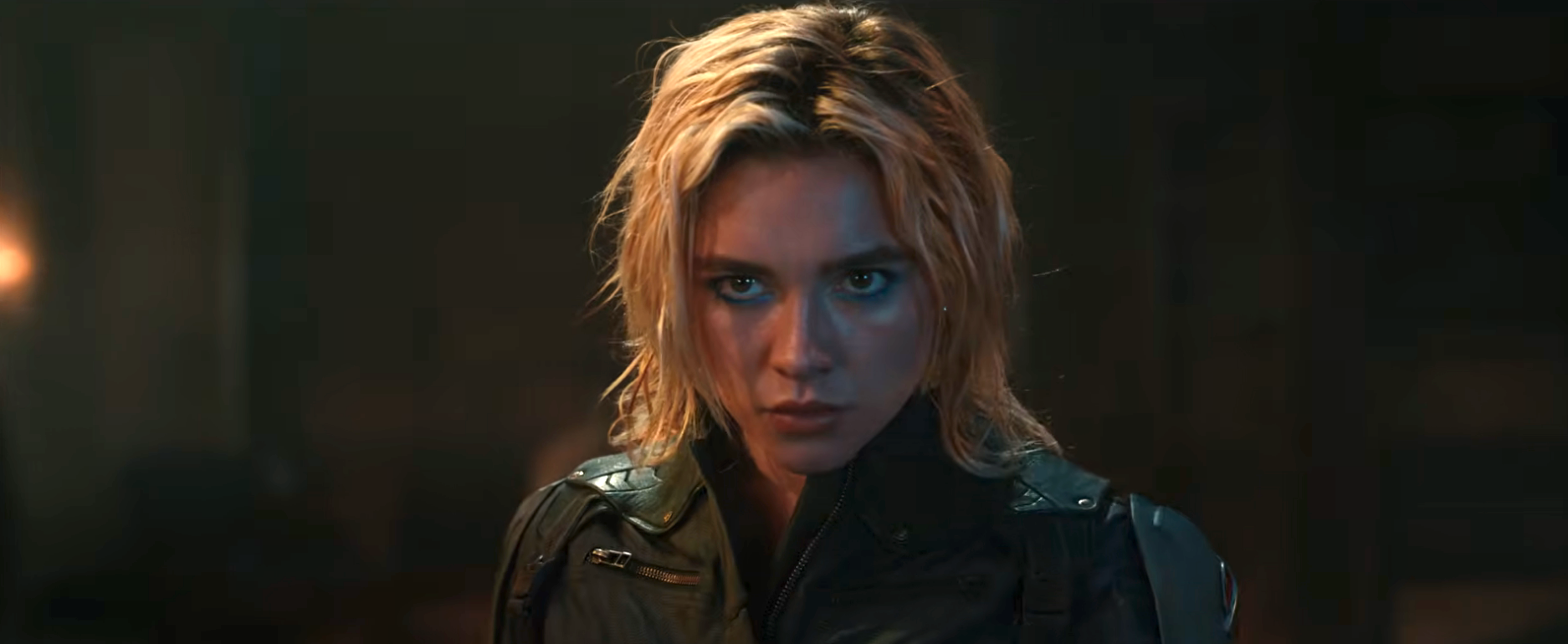A person with tousled hair looks intensely forward, wearing a military-style jacket, suggesting a dramatic scene