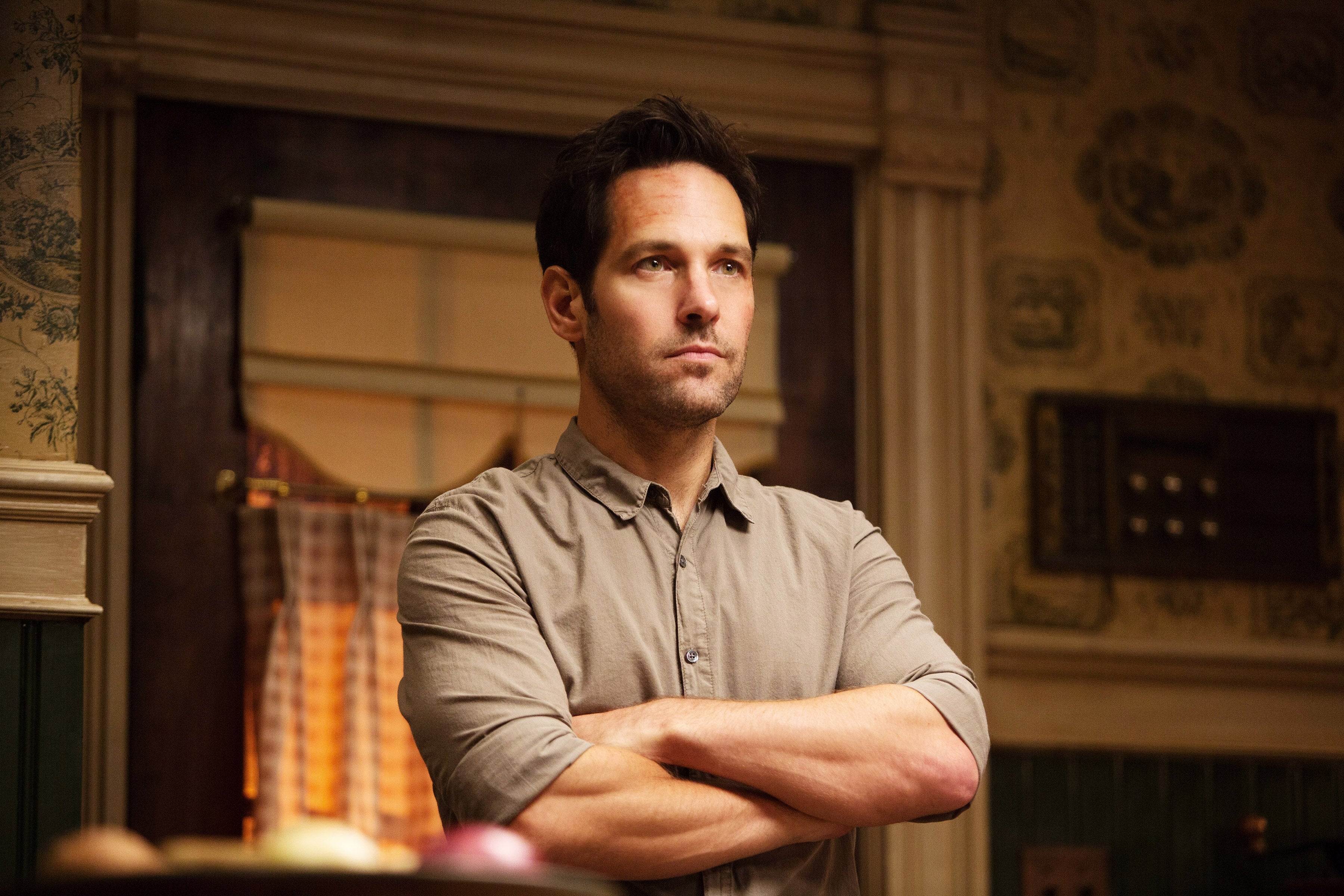 A person stands with folded arms in a warmly lit kitchen, looking thoughtful