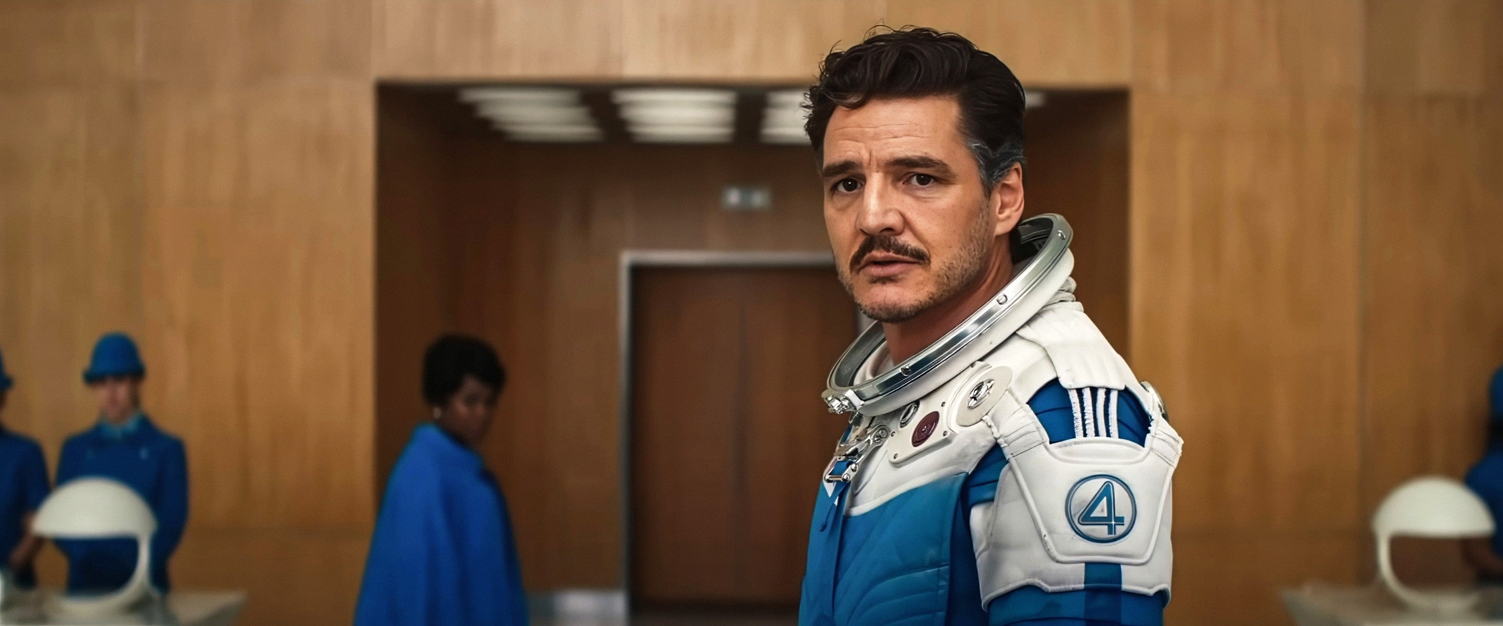 A person in a blue and white astronaut uniform stands in a wood-paneled room, with two people in blue uniforms in the background