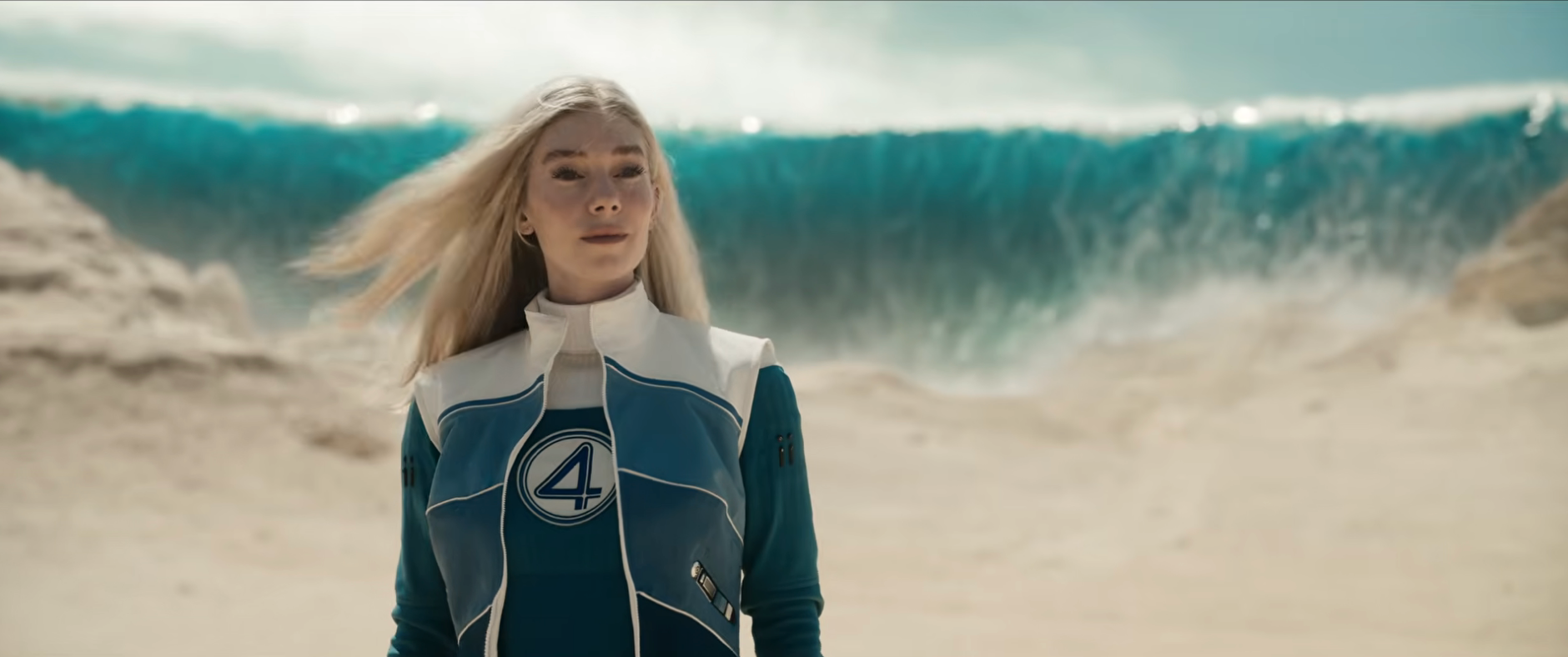 Person in a futuristic suit with a "4" emblem stands on a sandy beach, with a large wave in the background