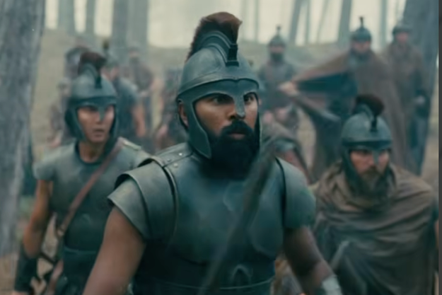 Actors dressed as ancient soldiers in helmets and armor, walking through a forest