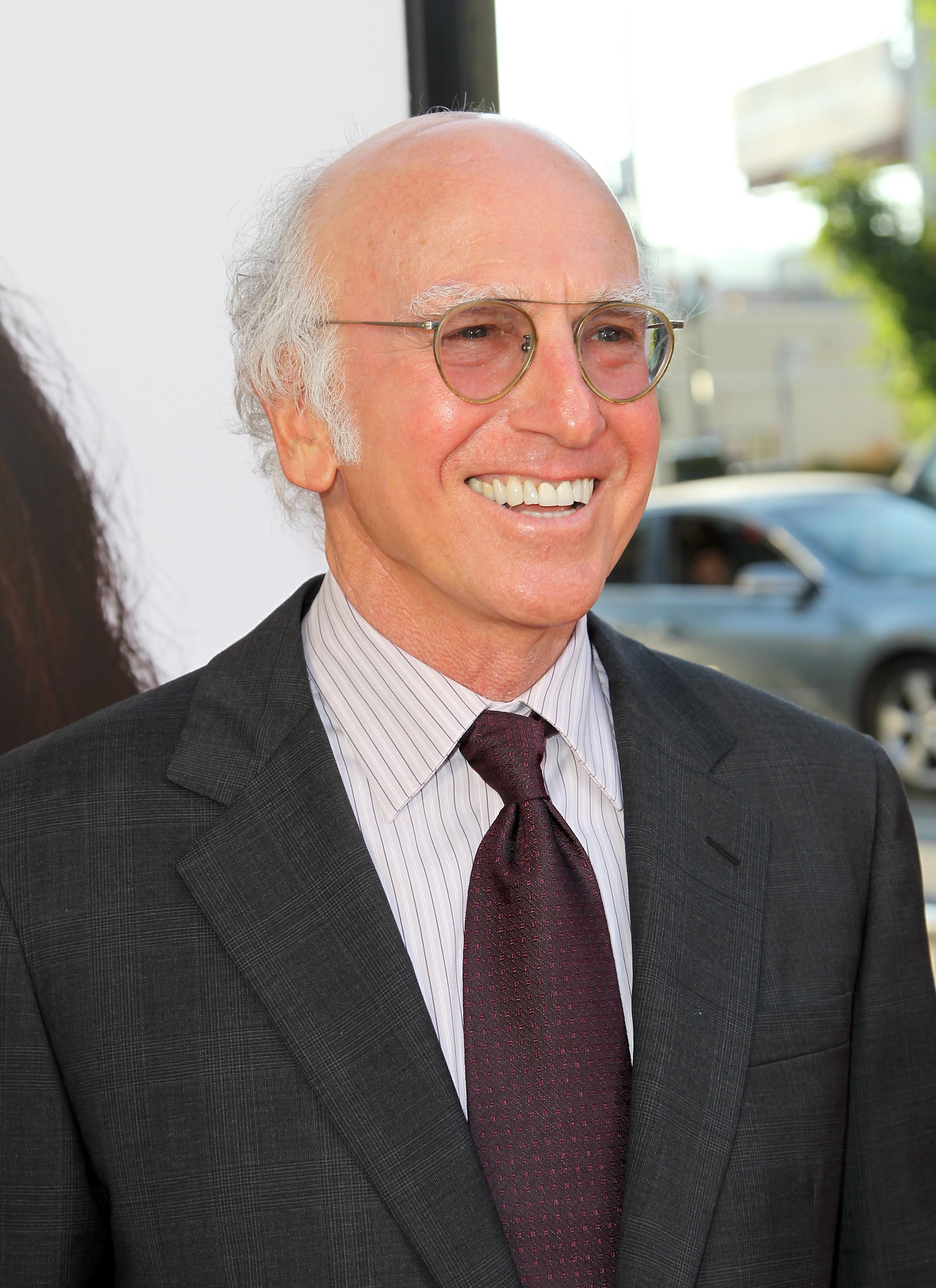 Person in a suit and tie smiles at an event, wearing round glasses