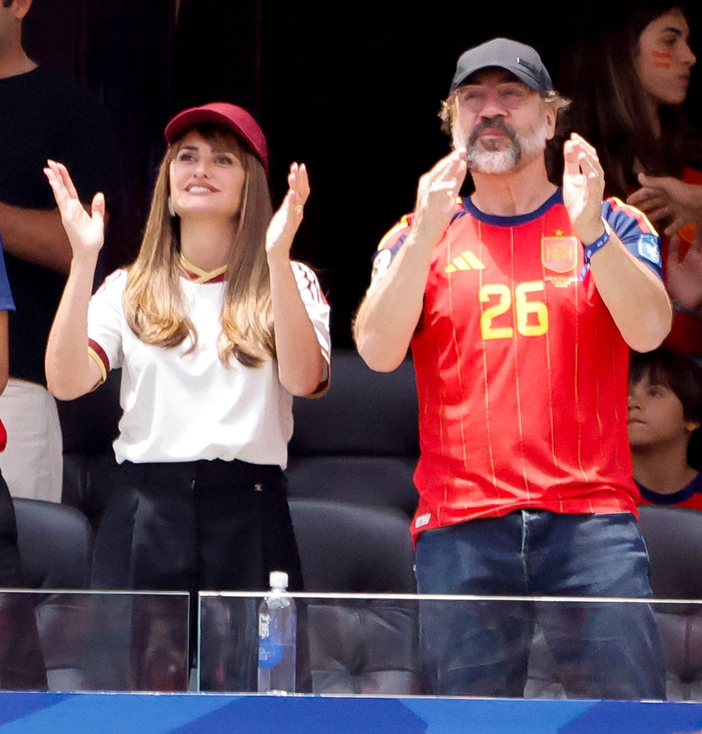 People in sports jerseys cheering at a stadium. They're excited and attentive to the action on the field