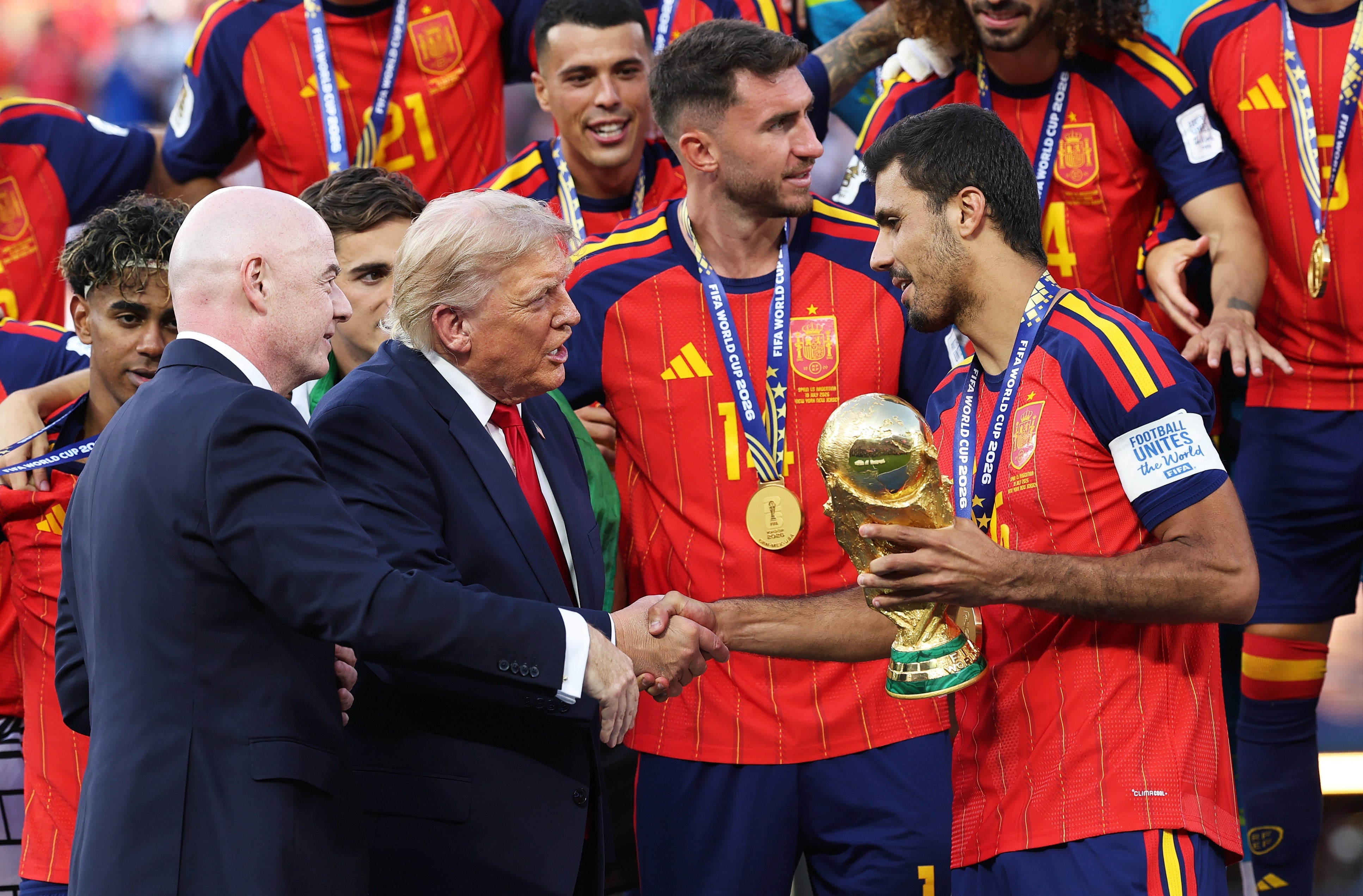Soccer team celebrates winning the championship trophy, shaking hands with officials. Players wear medals and uniforms
