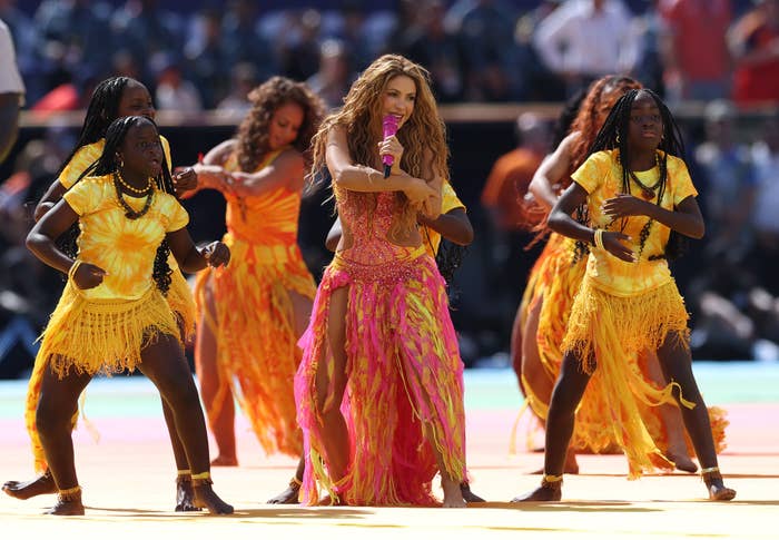 Performers in vibrant, fringed outfits dance energetically on stage during a live performance