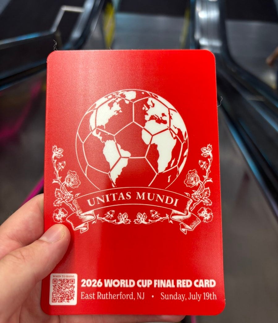 Hand holding a red card with "2026 World Cup Final Red Card" and details, featuring a globe shaped like a soccer ball with "Unitas Mundi" below it