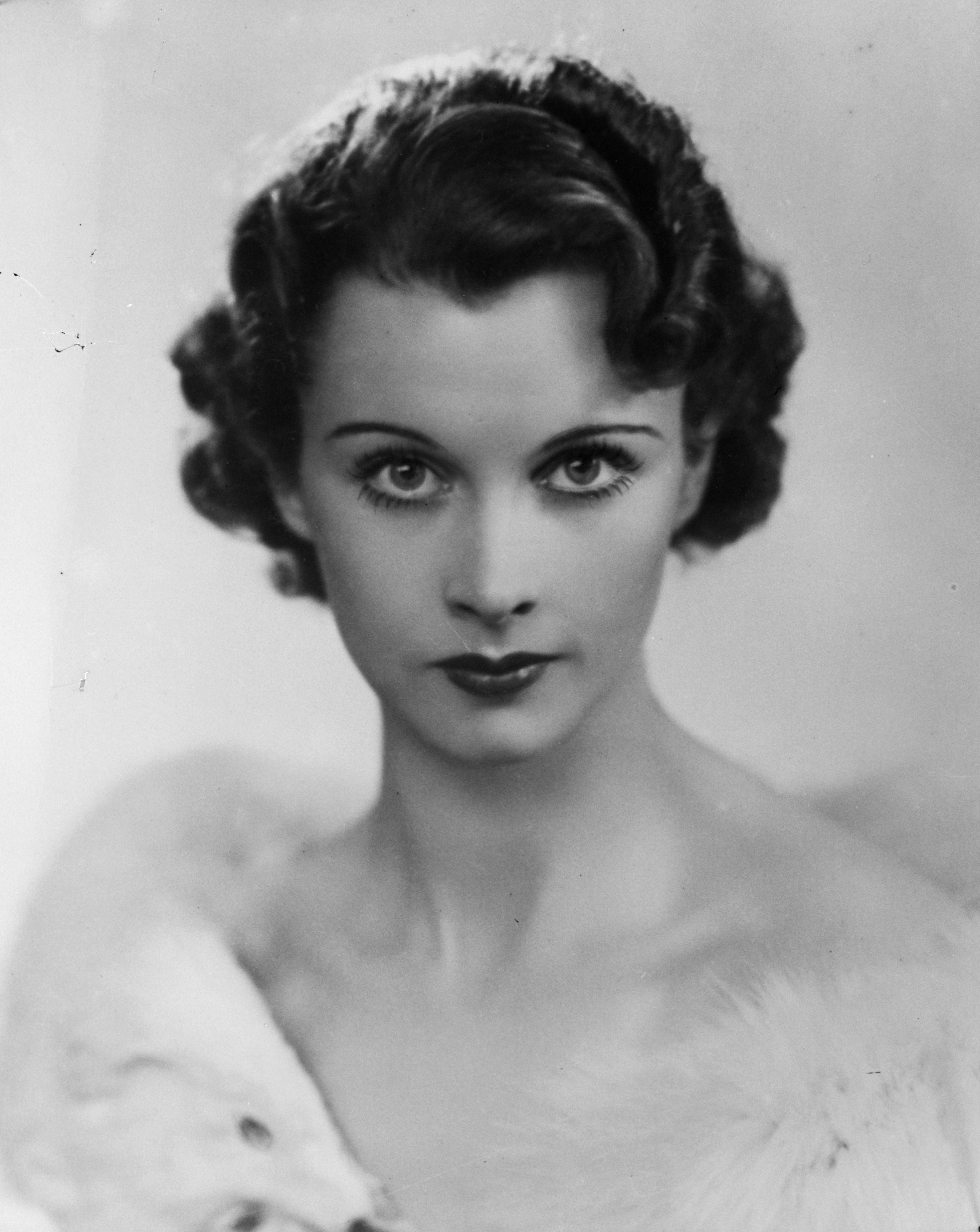 Vivian Leigh with styled curls gazes intently, wearing a fur shawl, capturing an early 20th-century glamour look