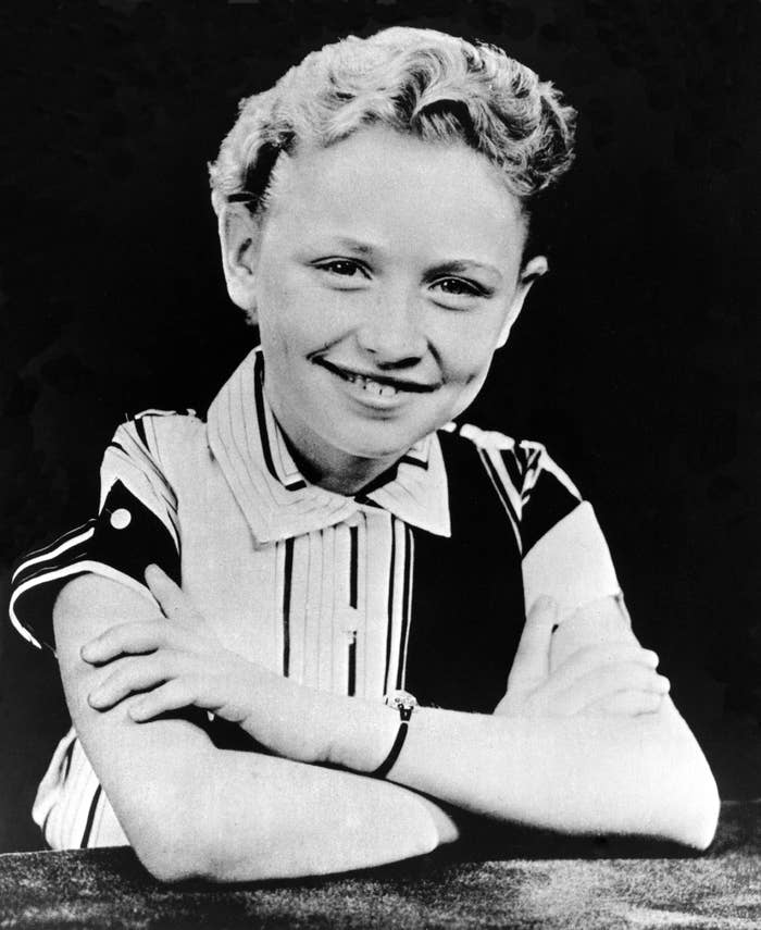 A 12-year-old Dolly Partonsmiling, arms crossed, wearing a striped shirt. Classic publicity photo from an earlier era.