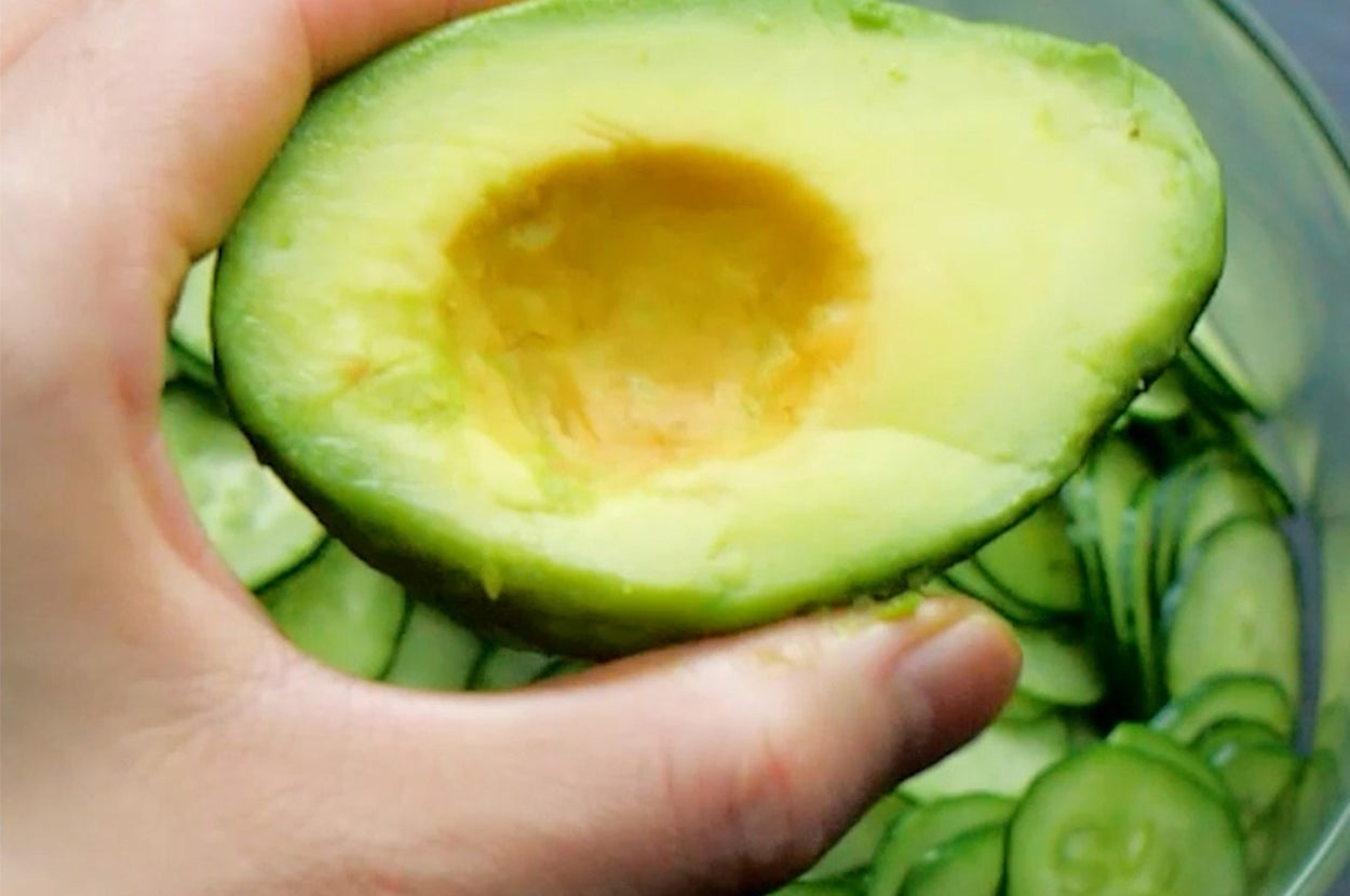 手に持ったカットしたアボカドとスライスされたキュウリのボウル。