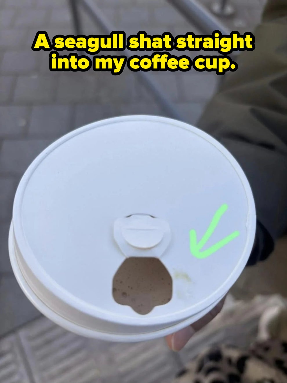 Coffee cup lid with a small spill near the drinking hole. A green arrow points to a tiny stain