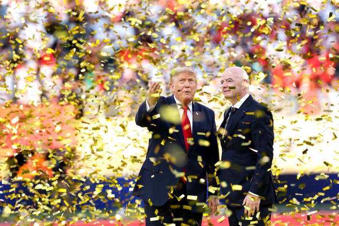 Two people stand amid a shower of gold confetti, dressed in formal suits, at a sports event celebration