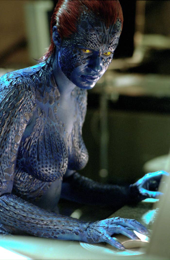 A character with intricate blue skin and a textured costume, sitting at a computer, appears focused