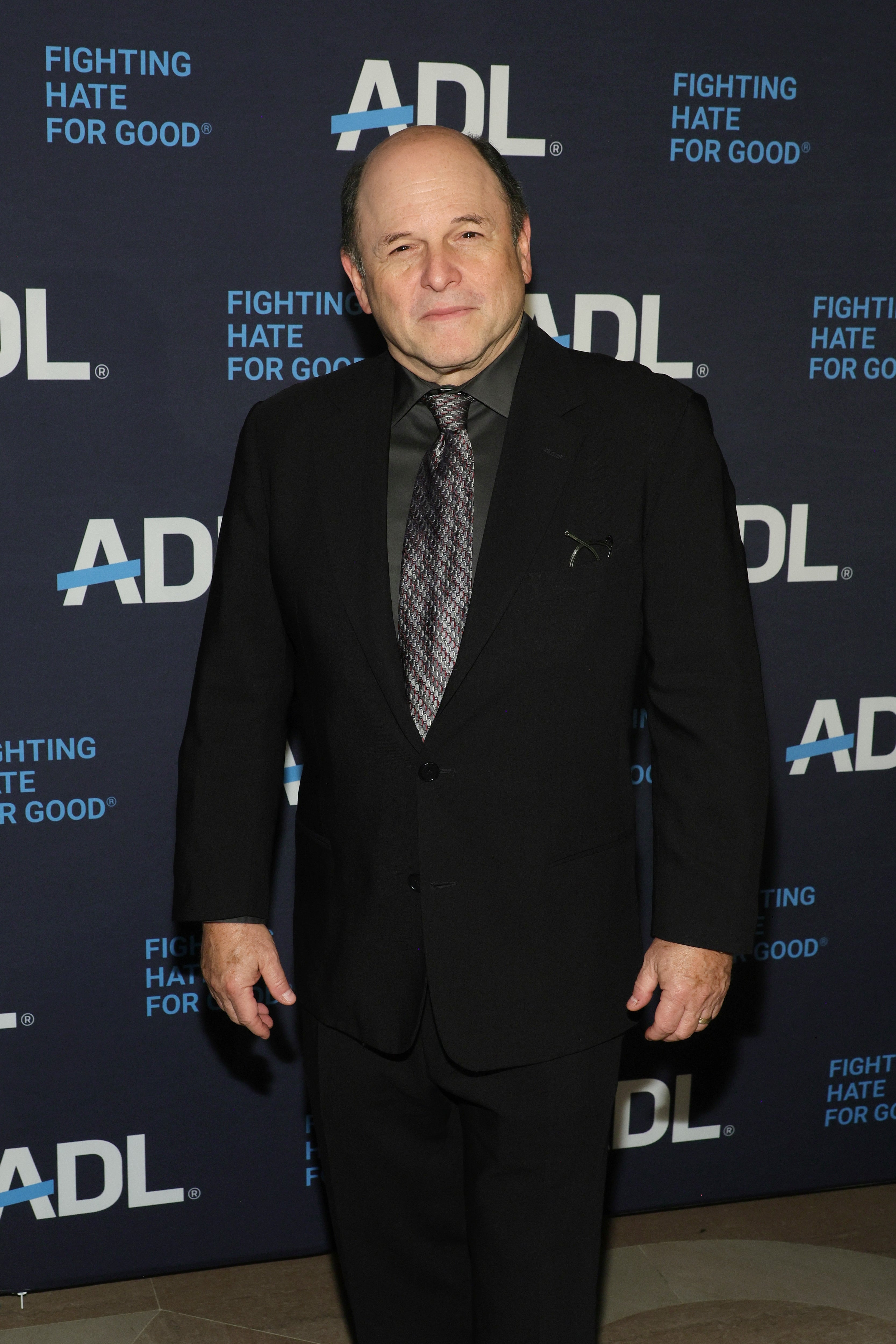 Person in a dark suit and tie at an ADL event against a backdrop with the slogan "Fighting Hate for Good."