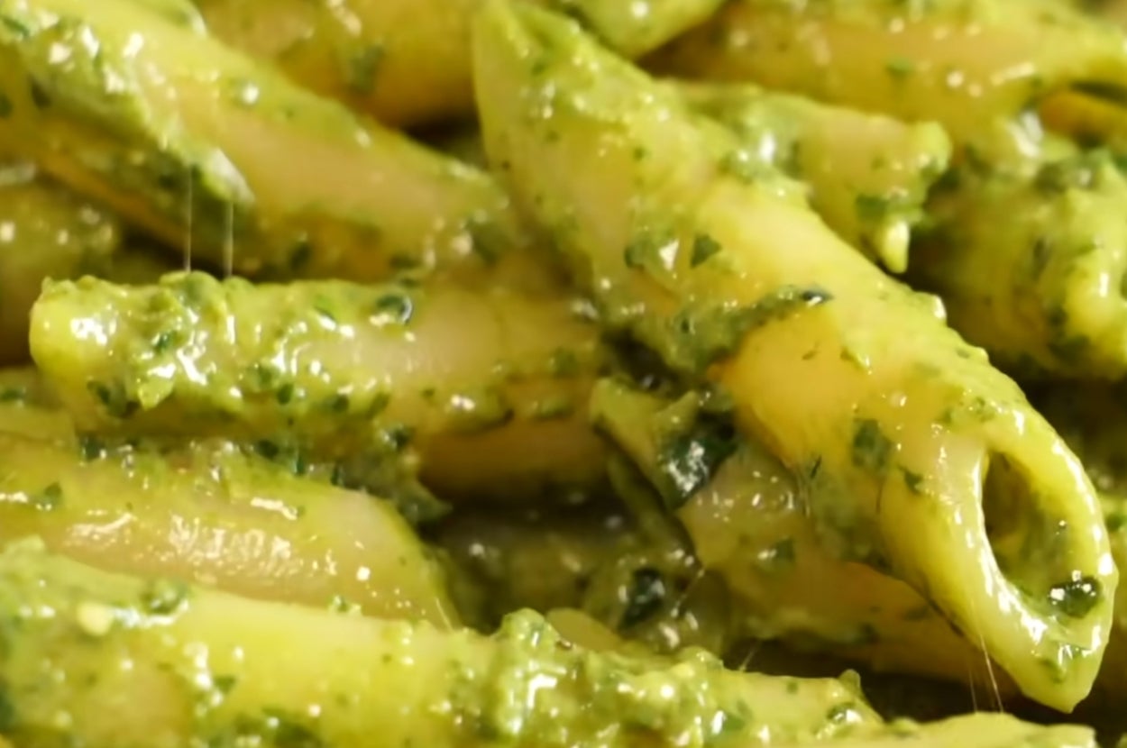 Penne pasta coated in creamy pesto sauce, garnished with visible herbs