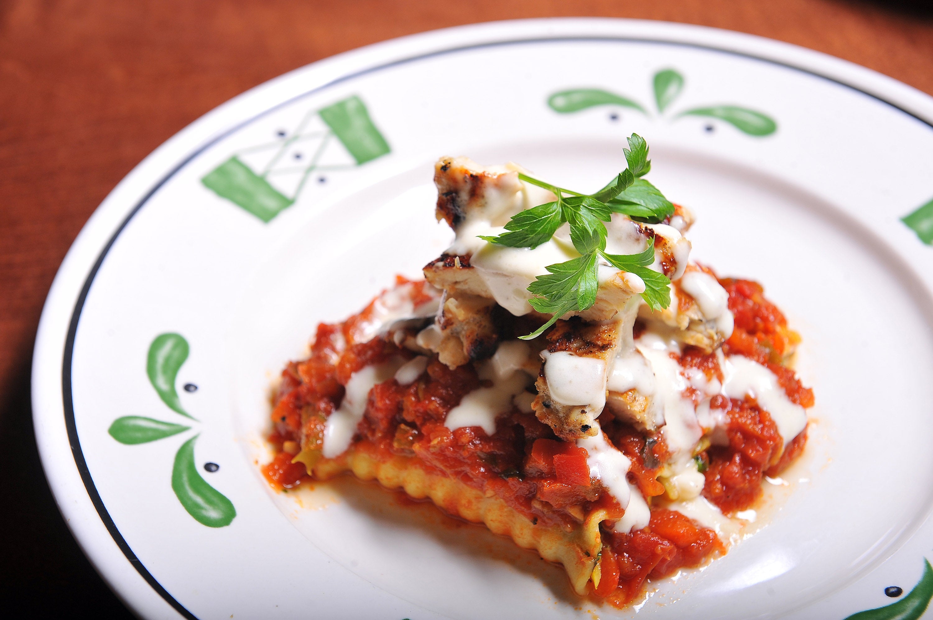 A sheet of lasagna topped with condiment and a parsley garnish connected patterned dinnerware