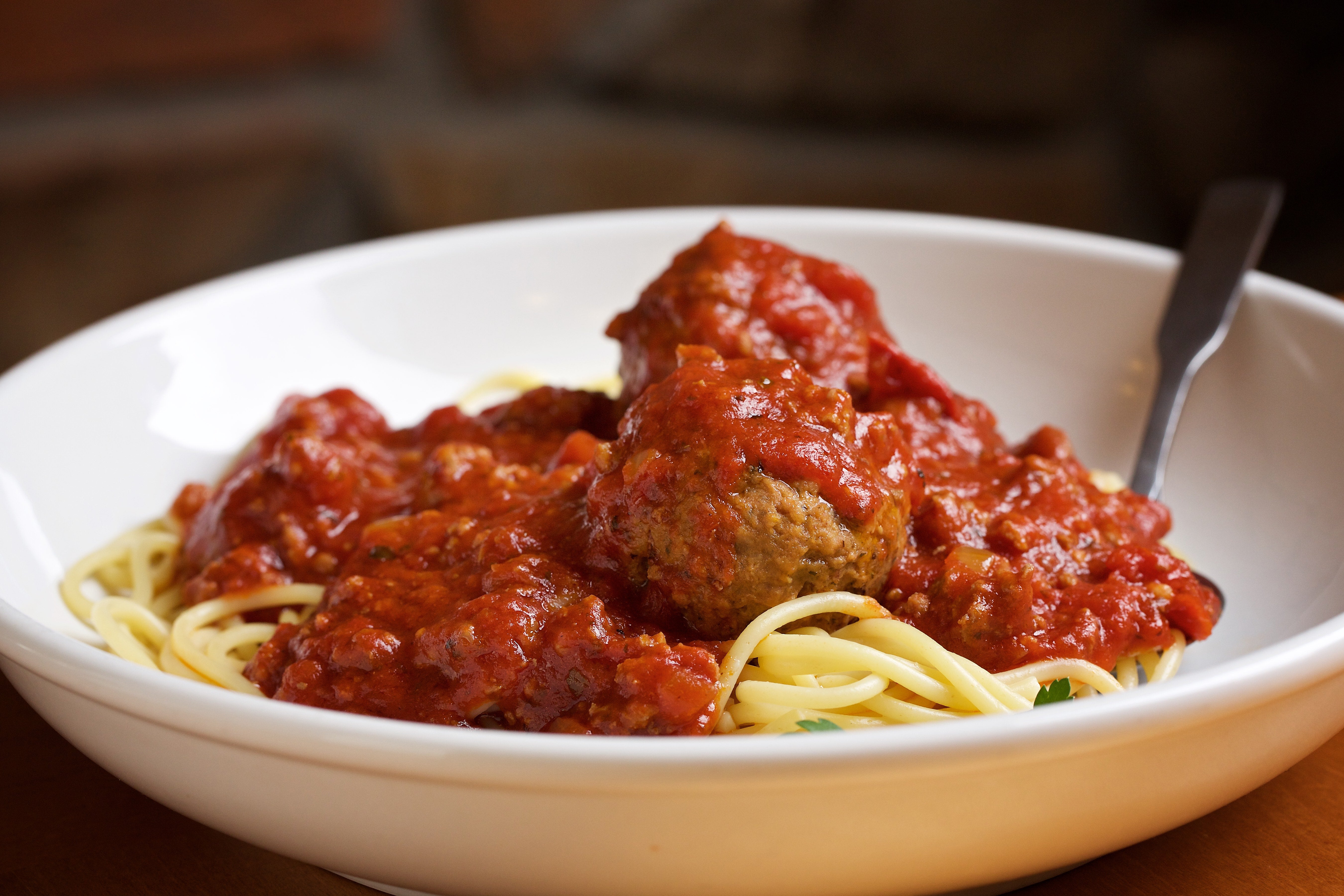 A sheet of spaghetti topped with marinara condiment and meatballs, presented with a fork successful a achromatic bowl