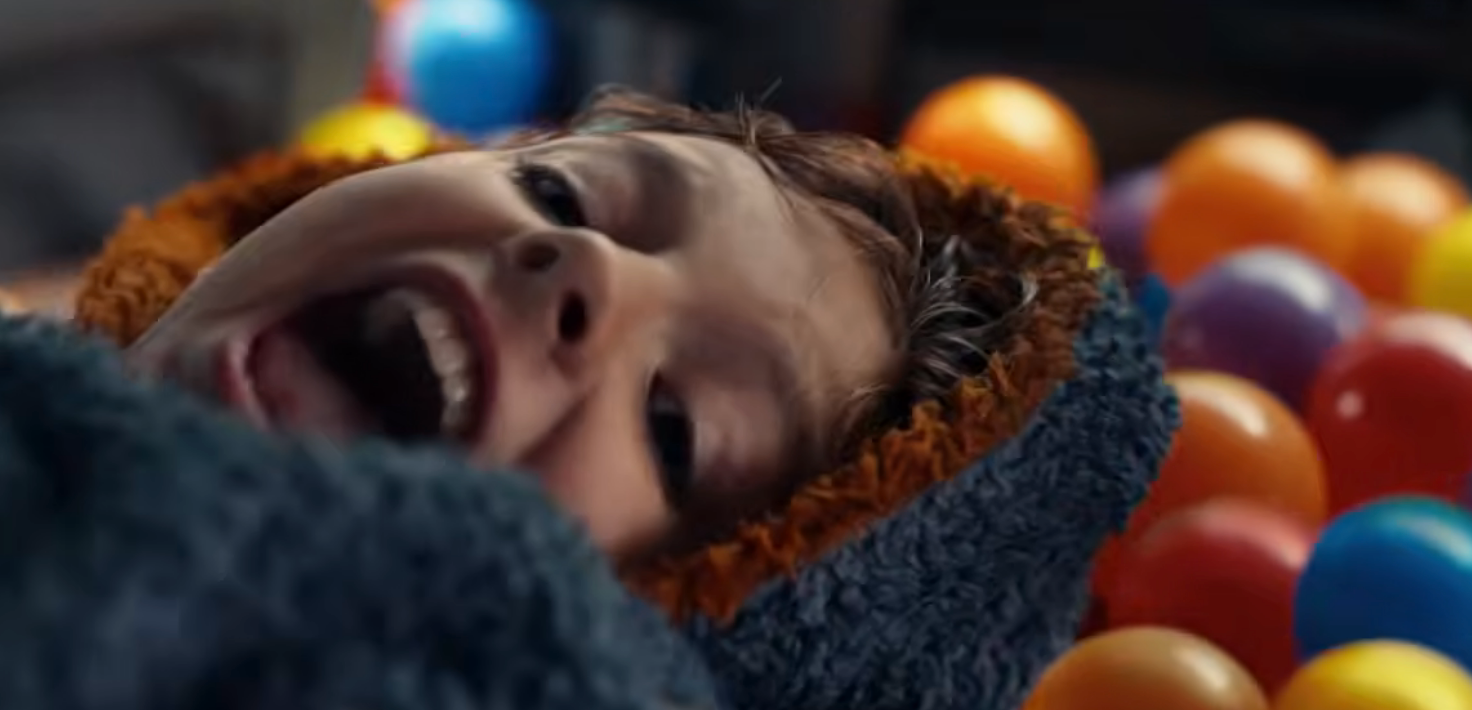 Child laughing joyfully while lying on a bed of colorful plastic balls