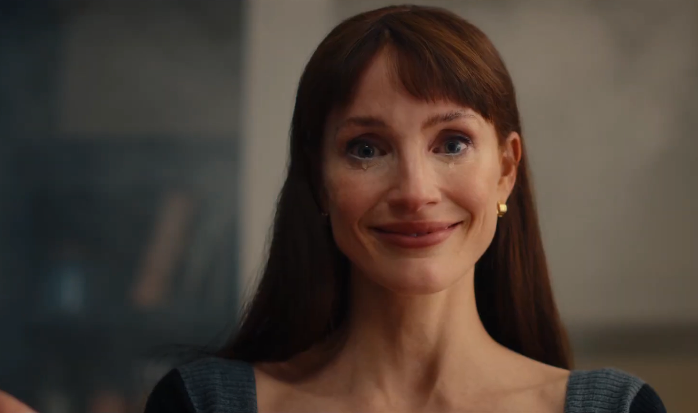 Smiling woman with long hair, gold earrings, wearing a stylish dress, appears emotional in a scene from a TV or movie
