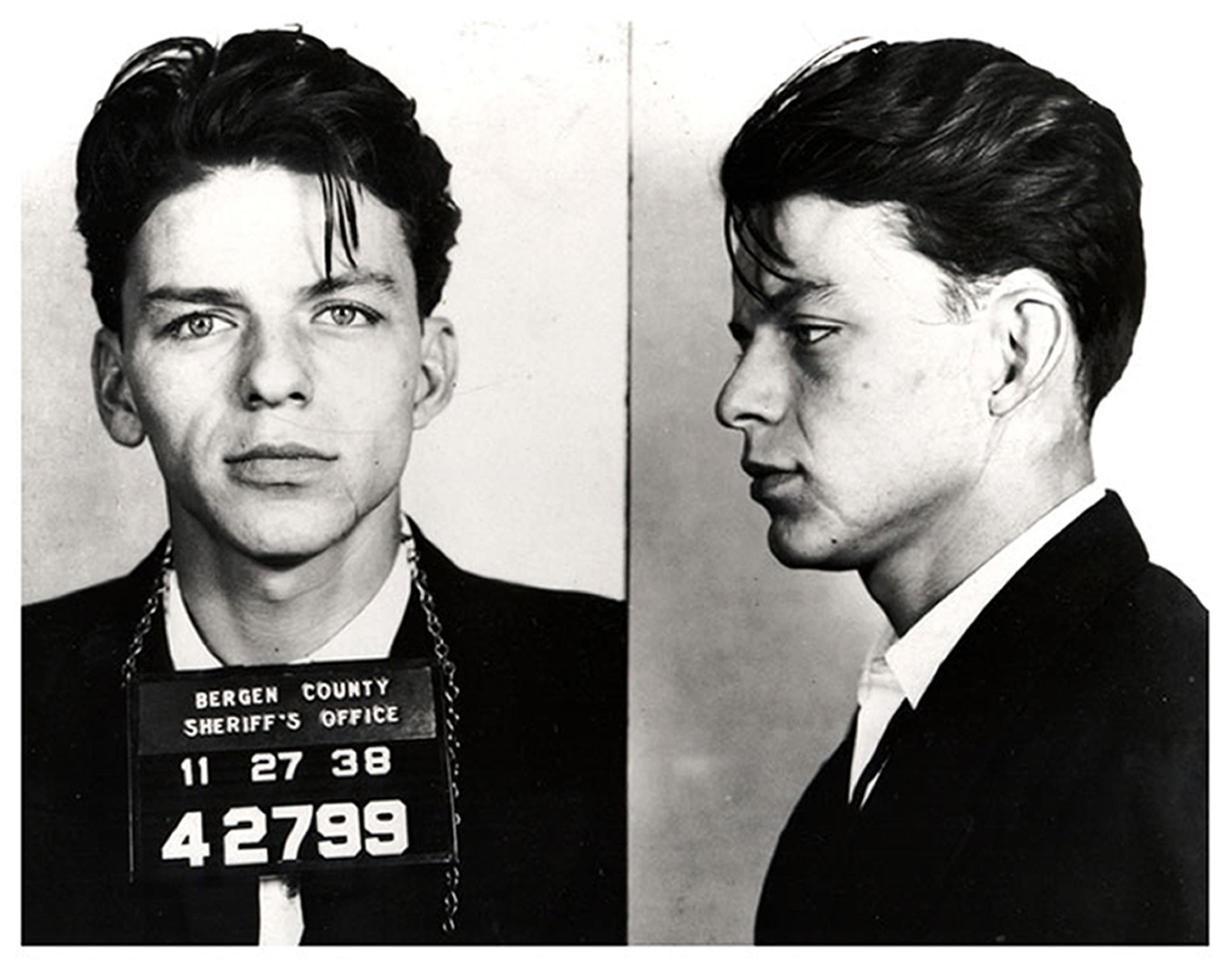 A historical mugshot of a young Frank Sinatra, dressed in a suit, with his hair slicked back, holding a sign with arrest details from Bergen County Sheriff's Office