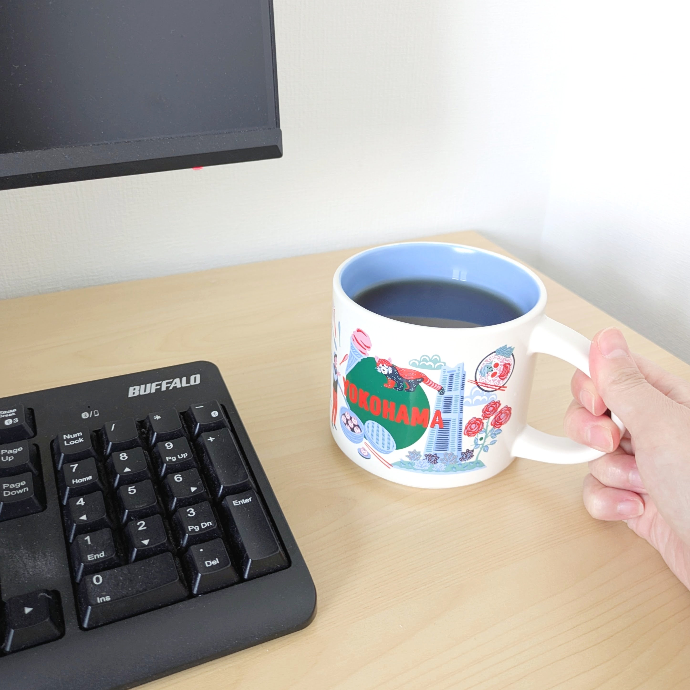 スターバックス「Discovery Series マグYOKOHAMA414ml」パソコンの横にある「YOKOHAMA」デザインのマグカップを持つ手。