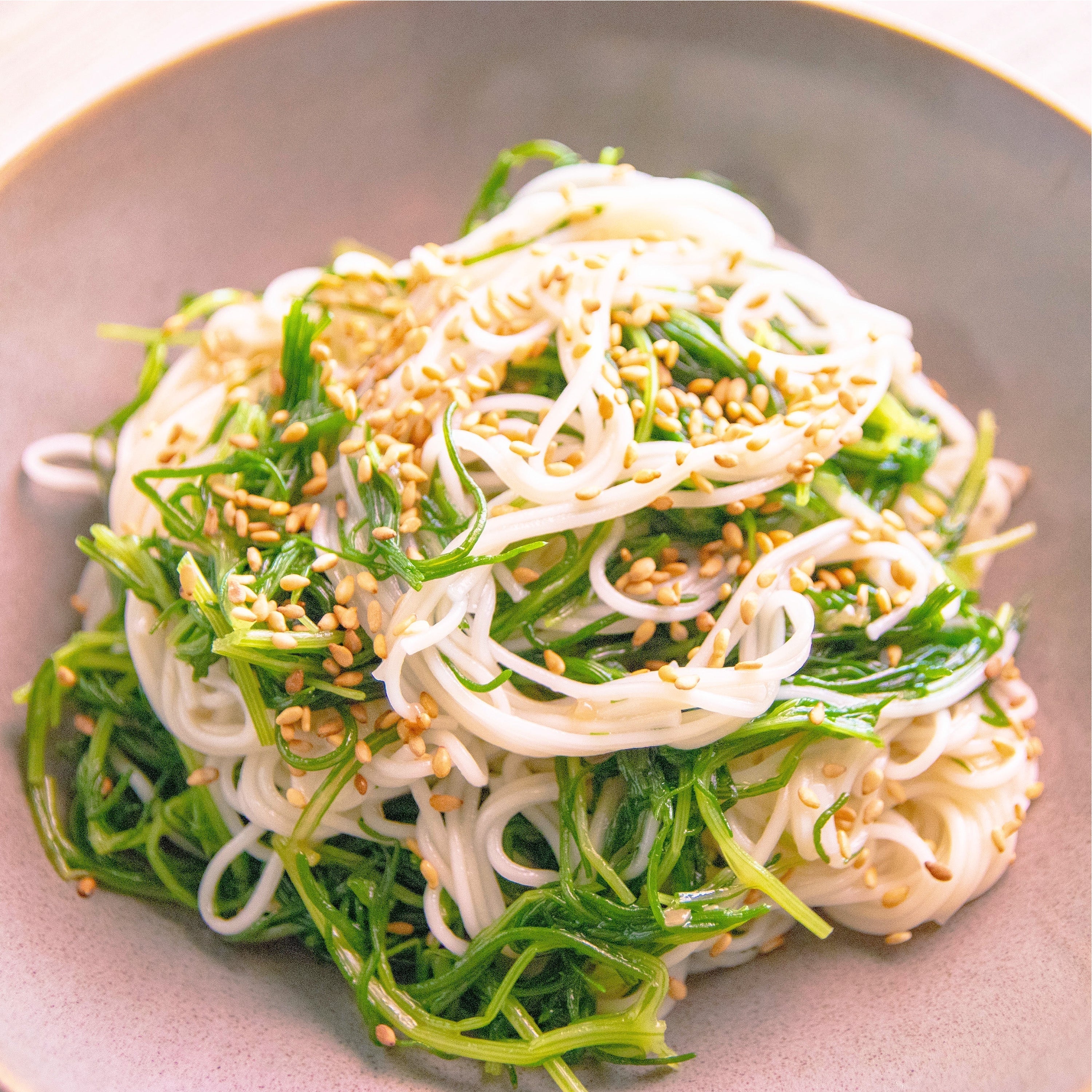 お皿に盛られた冷たい麺と海藻のサラダ、上にゴマがまぶされている。