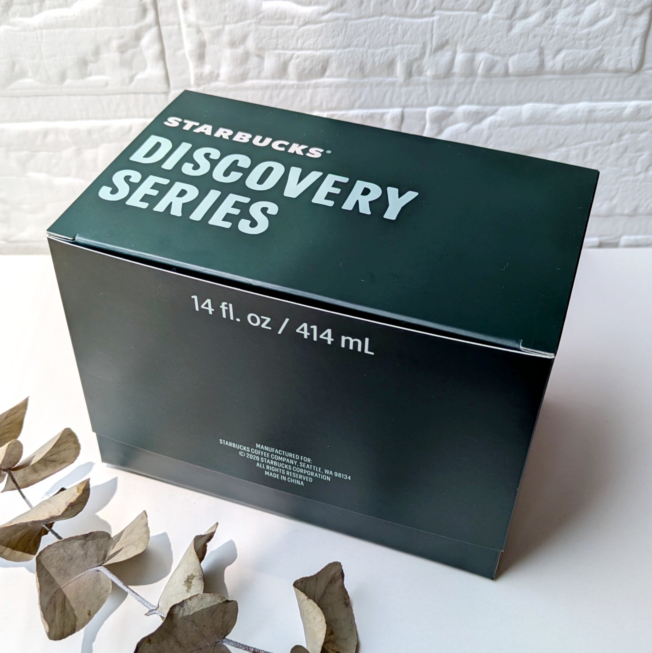 スターバックス「Discovery Series マグYOKOHAMA414ml」スターバックスのディスカバリーシリーズの箱（14 fl. oz / 414 mL）が置かれている様子。隣に乾燥した葉。