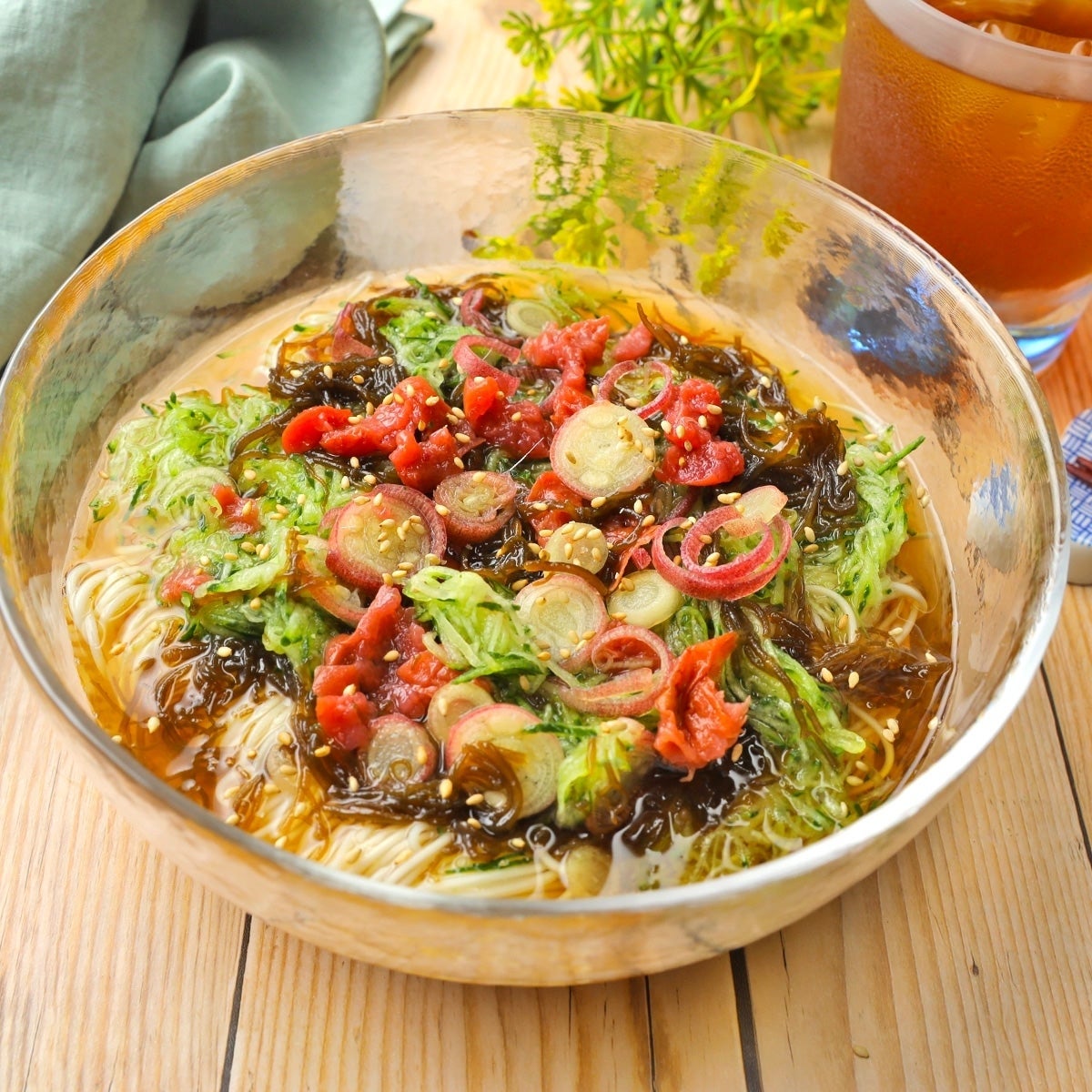 冷麦の上にたっぷりのわかめと野菜が盛り付けられた料理。横に冷たい飲み物が置かれている。