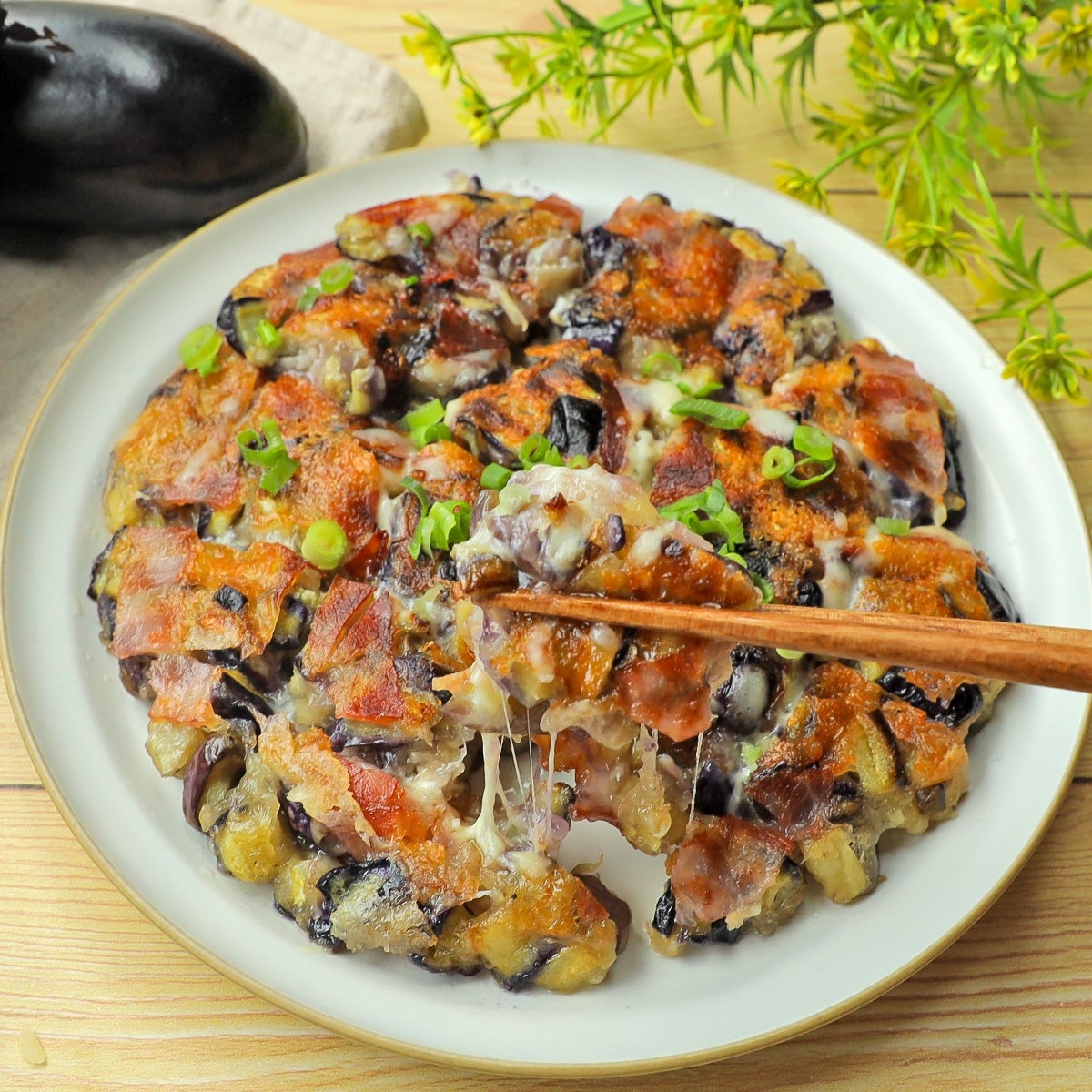 焼きナスとチーズのピザ風料理が皿に盛られ、上に小口ねぎがトッピングされています。