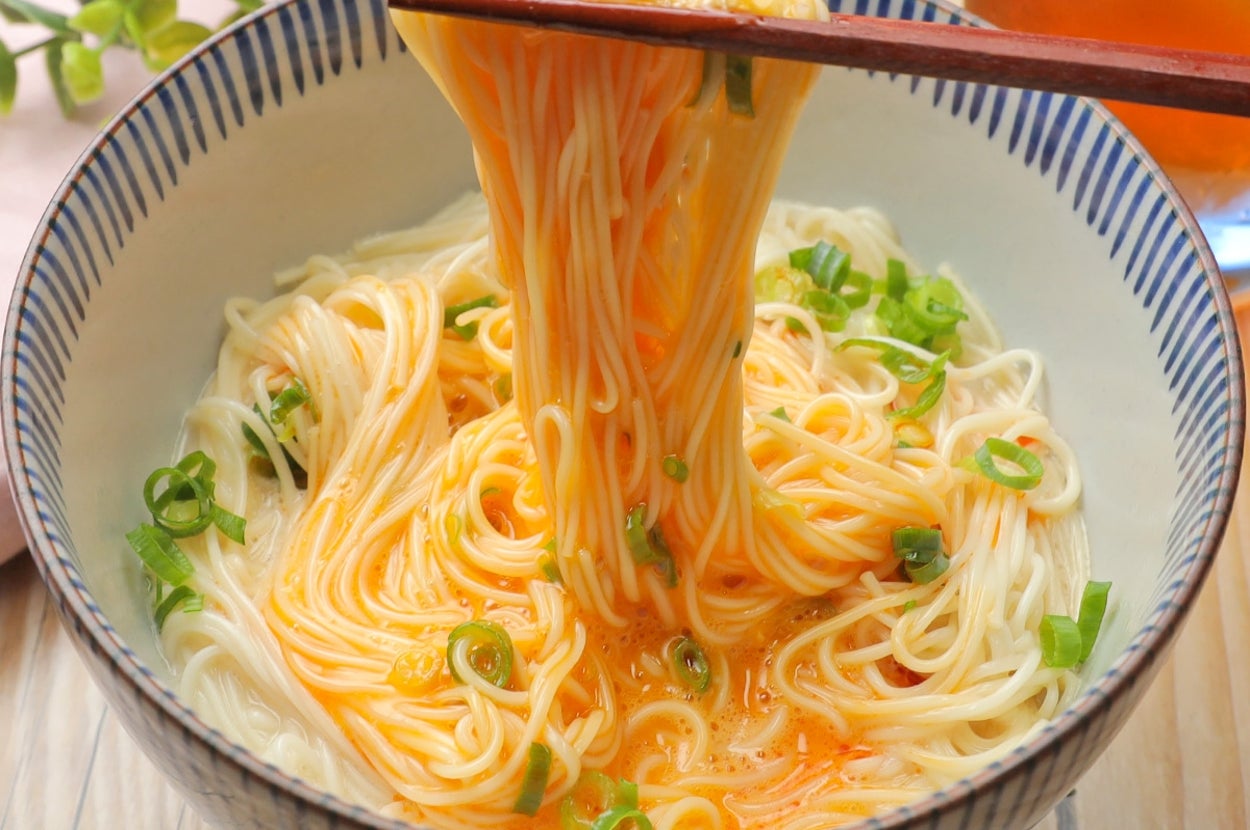 丼に盛られた麺を箸で持ち上げる様子。薬味として小ネギが散らされている。