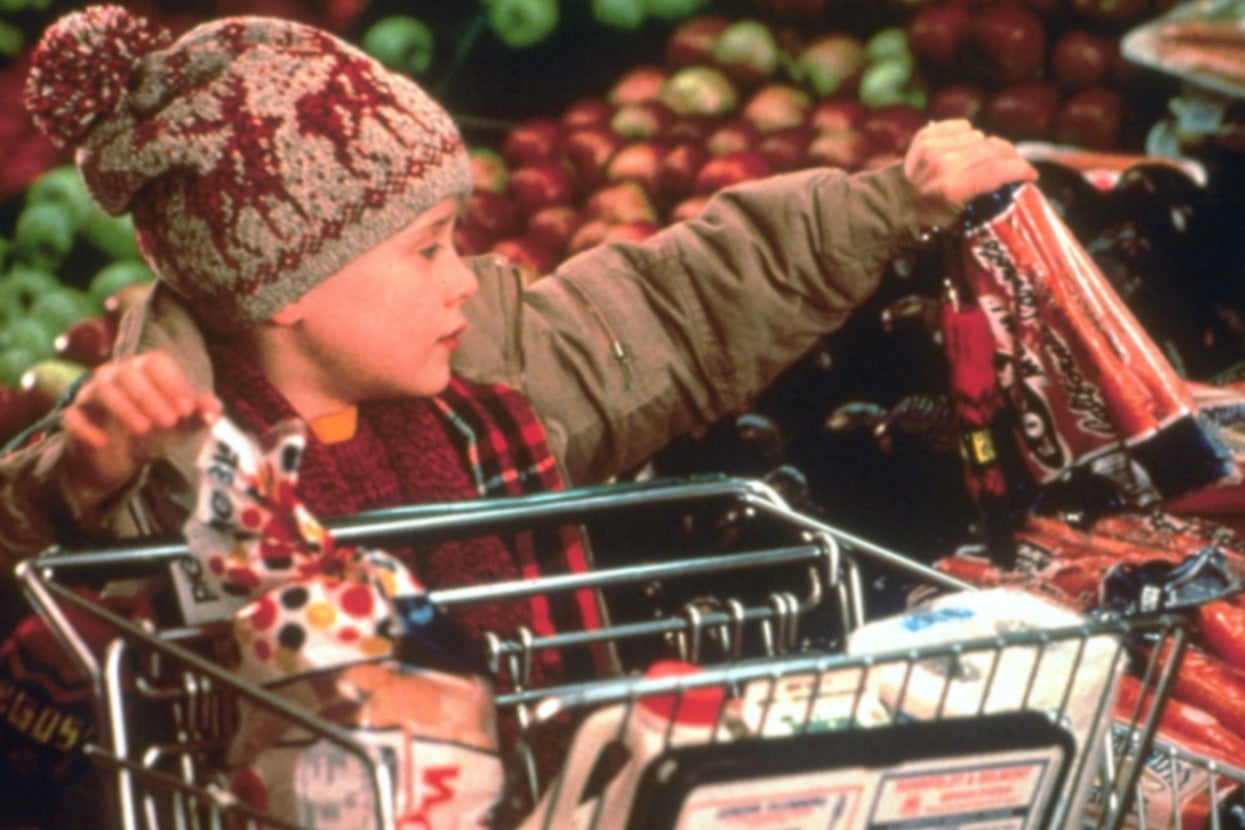 A child in warm winter clothing shopping for groceries, placing items into a cart in a store with a focus on food products