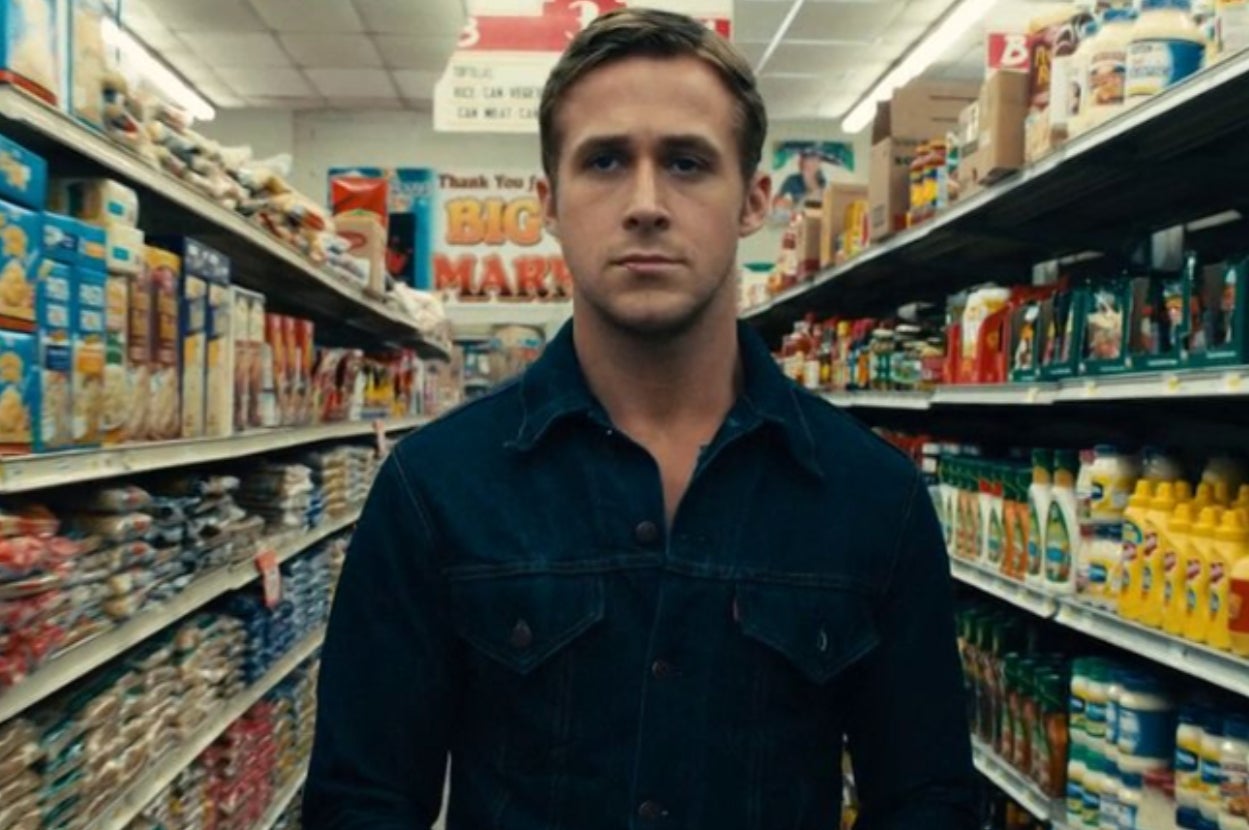 Person in a denim jacket stands in a supermarket aisle filled with groceries, looking forward