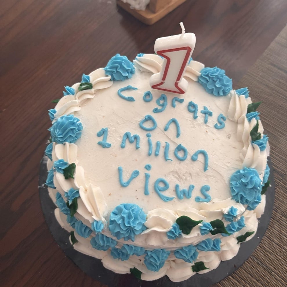Cake with blue and white icing reads "Congrats on 1 million views" topped with a candle shaped like the number one
