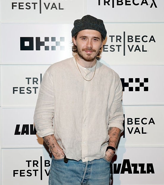 A person on a red carpet wears a casual outfit with a beanie, light shirt, and jeans at the Tribeca Festival backdrop