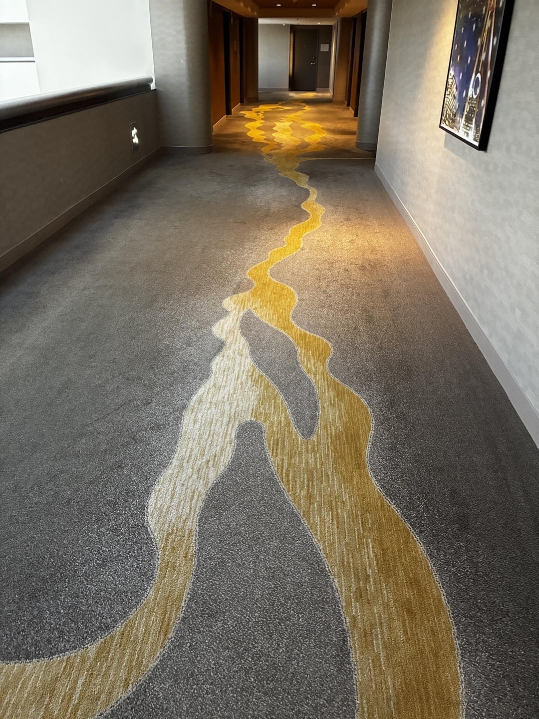 A hotel hallway carpet with an abstract yellow pattern resembling a winding river