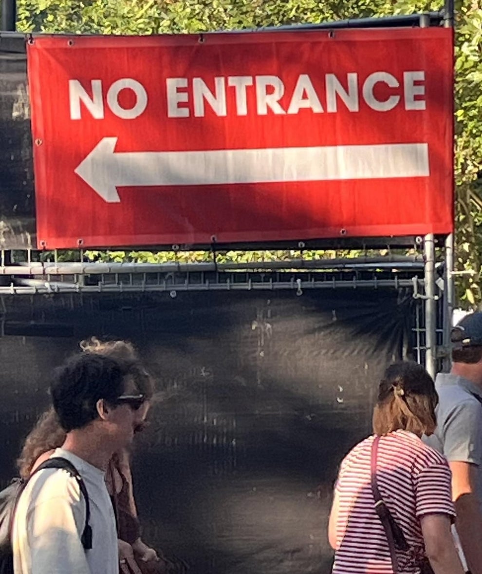 Sign with "No Entrance" and a left-pointing arrow, indicating restricted access. People walk nearby