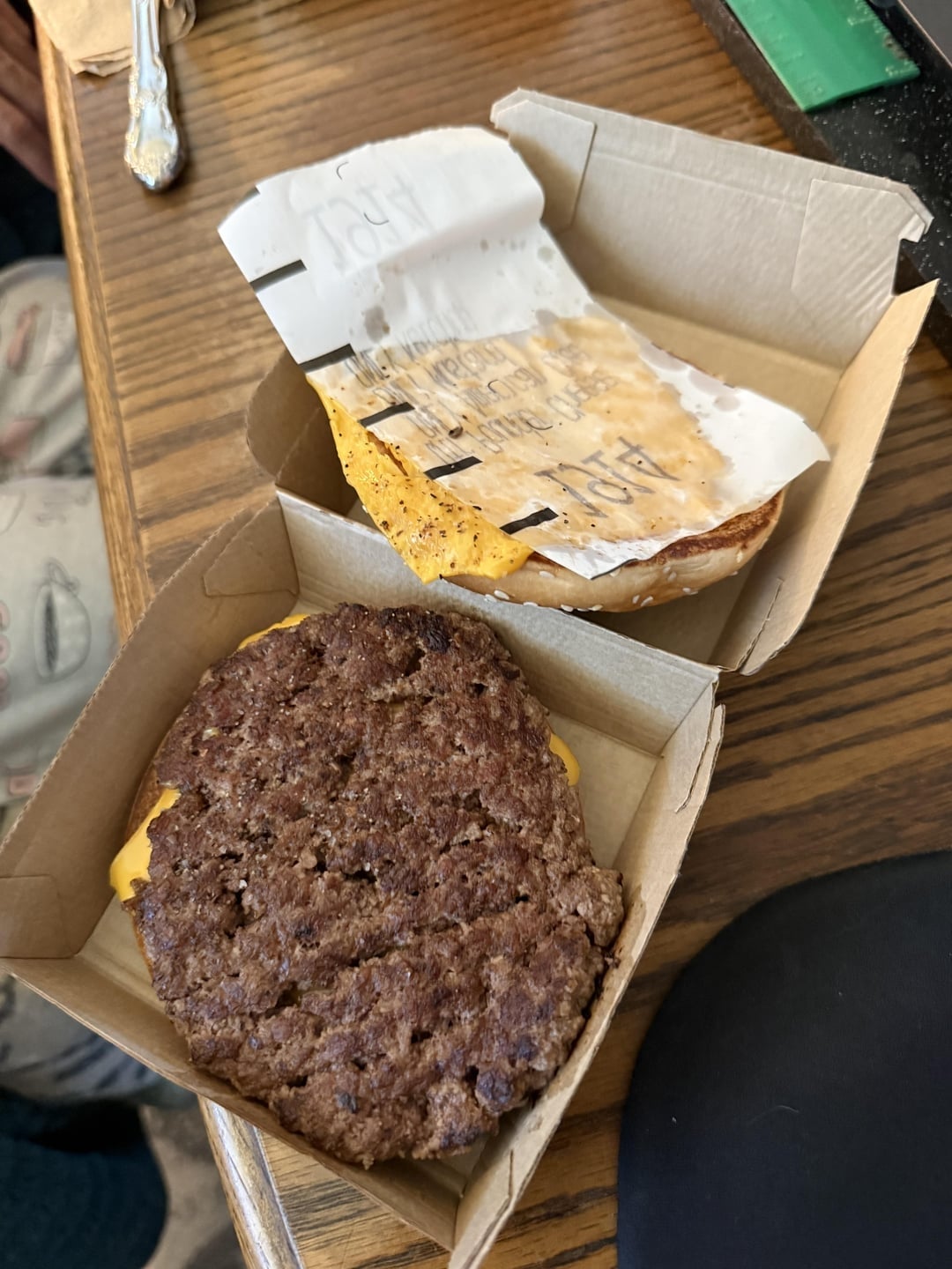 Open hamburger boxes with a burger patty and melted cheese in one box, and a bun with cheese sticking to the wrapper in the other box