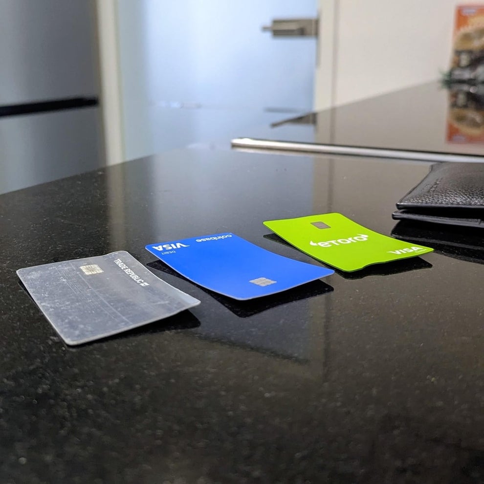 Three credit cards, each a different design, are displayed on a dark countertop next to a black wallet. A blurred kitchen background is visible