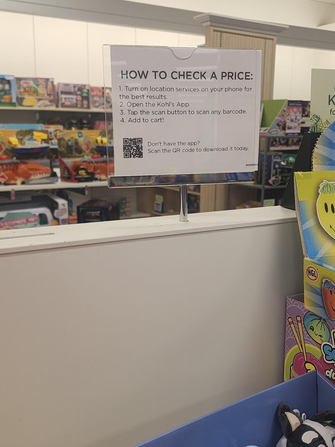 Sign in a store with steps to check a price using Kohl's app: turn on location, open the app, tap to scan, and add to cart. QR code for app download