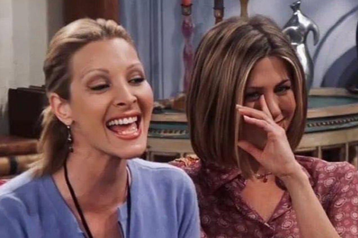 Two women laughing together, one in a light blouse with a ponytail, the other with a bob haircut in a patterned top, sitting indoors