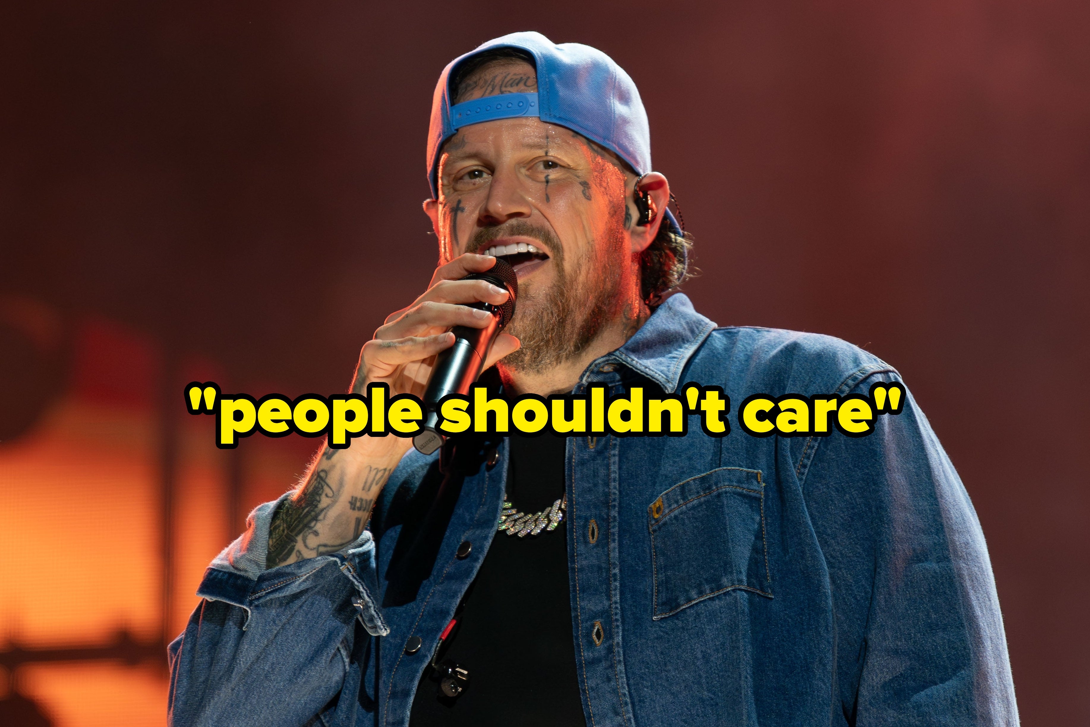 Jelly Roll  performing on stage, wearing a denim jacket and cap, holding a microphone, with a warm-lit backdrop