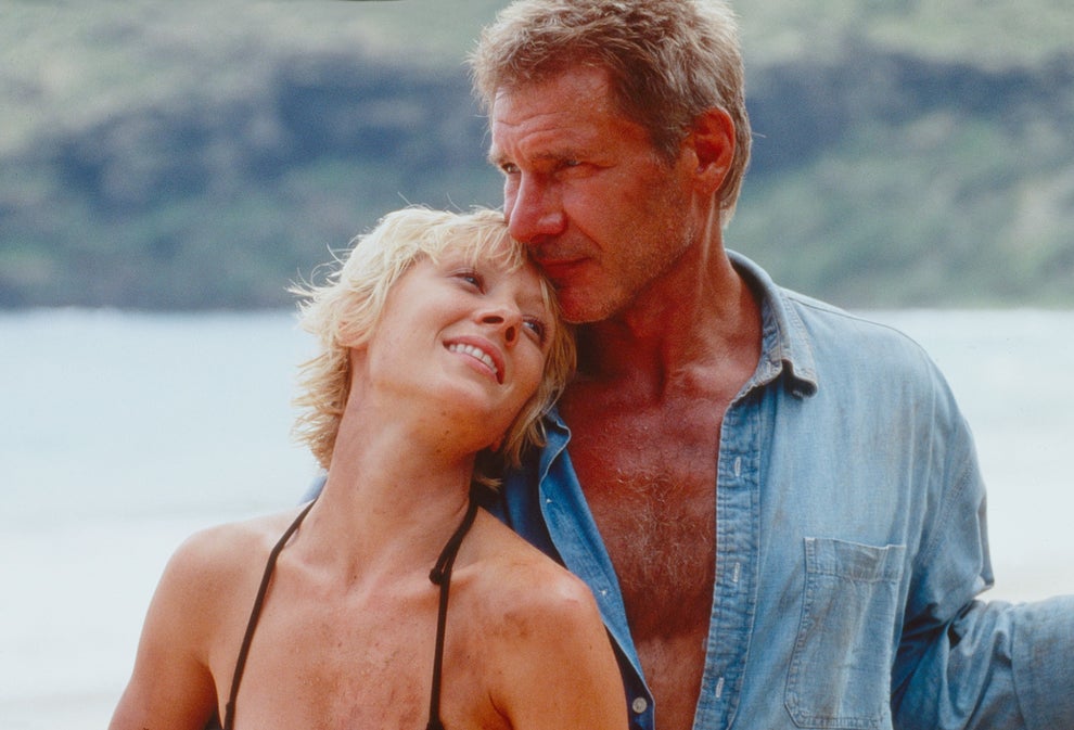 A couple is on a beach, smiling and embracing. The man is wearing a buttoned-down shirt