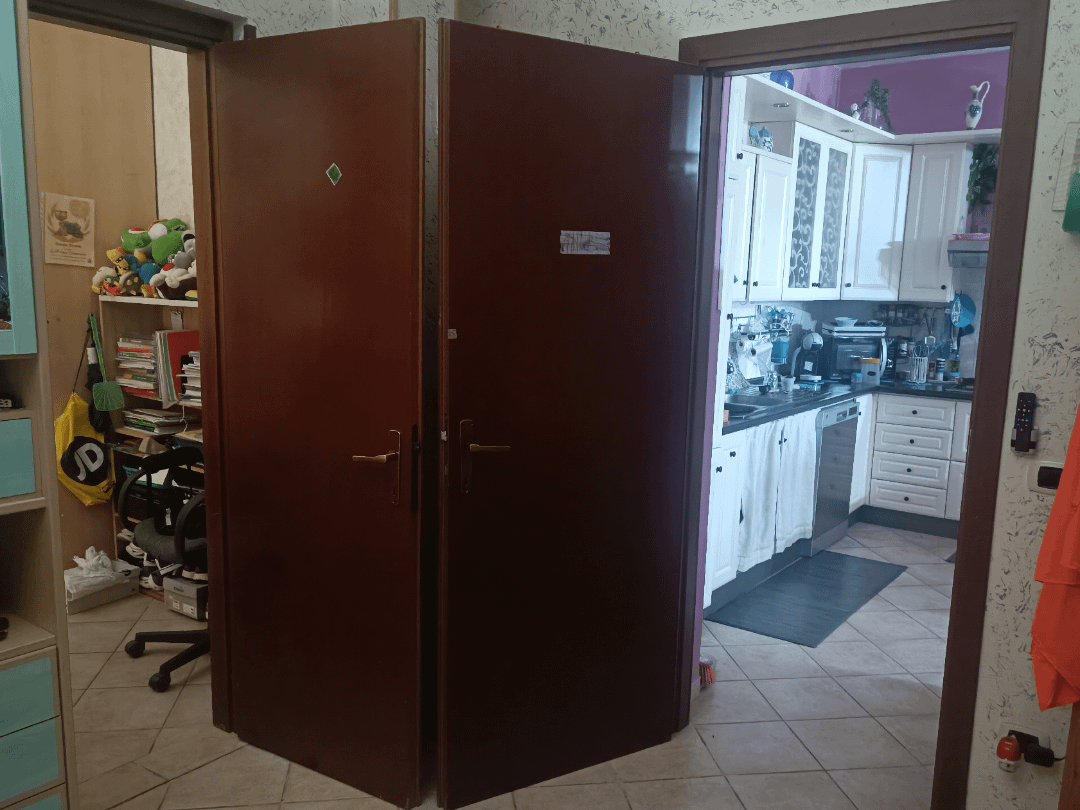 Buka pintu ganda yang mengarah dari kantor yang berantakan ke dapur yang rapi. Rak-rak berisi mainan dan buku terlihat di kantor